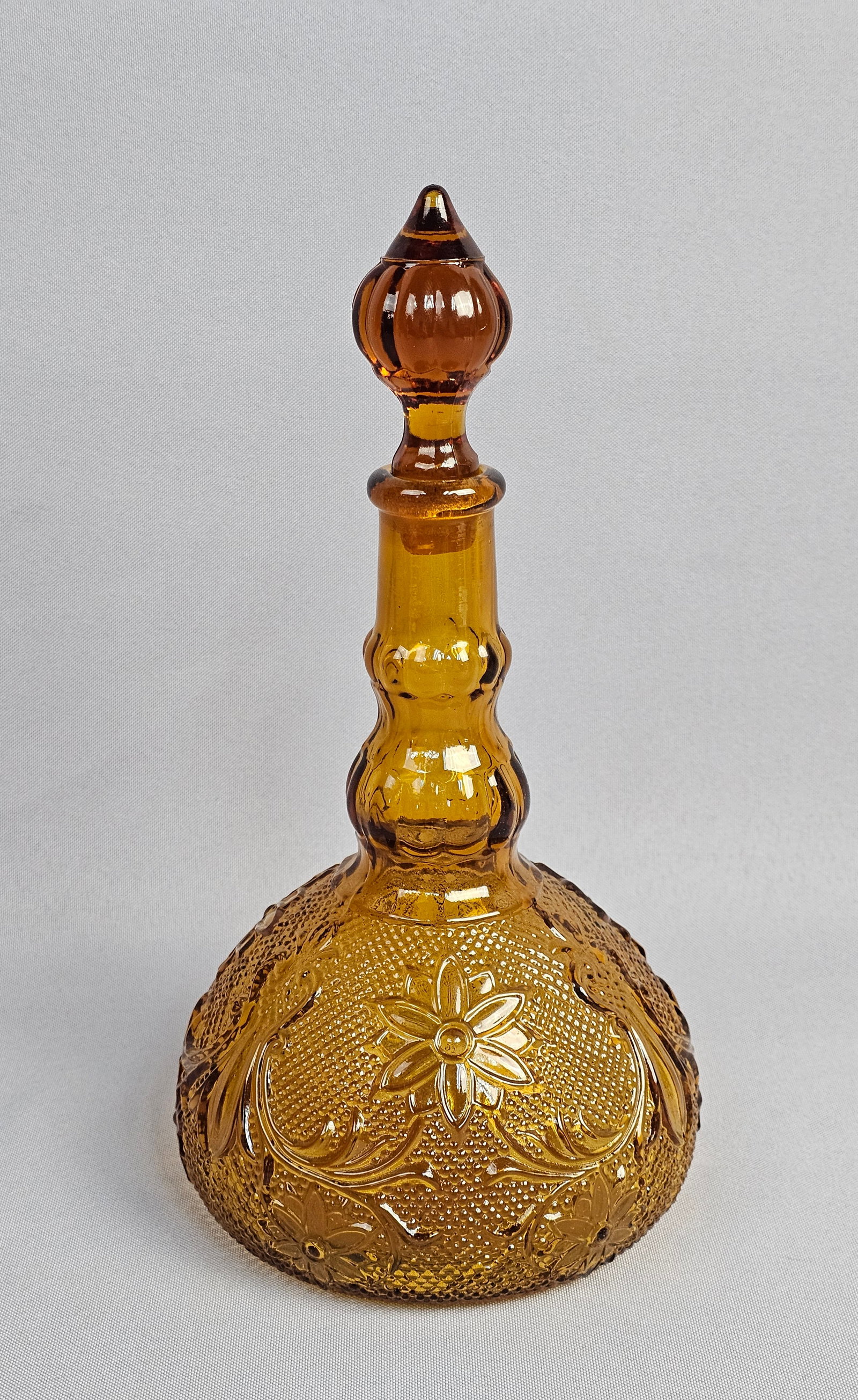 Indiana Glass Amber Sandwich Pattern Decanter with Stopper: This amber-colored pressed glass decanter is designed in the Sandwich pattern, produced by Indiana Glass and distributed by Tiara Exclusives. The vessel features a bulbous body with an embossed design