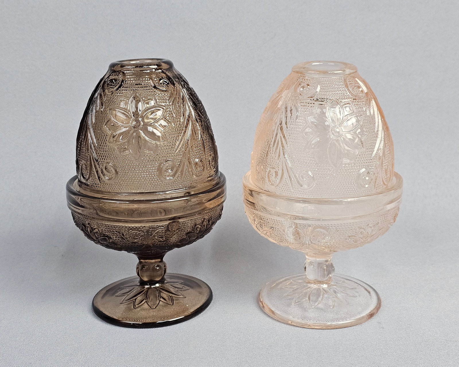 A Pair of Tiara Indiana Glass Sandwich Pattern Fairy Lamps: A pair of two-piece pressed glass fairy lamps in the Sandwich pattern, produced by Indiana Glass for Tiara Exclusives. The set includes one smoky topaz brown lamp and one pale rosaline pink lamp. Each