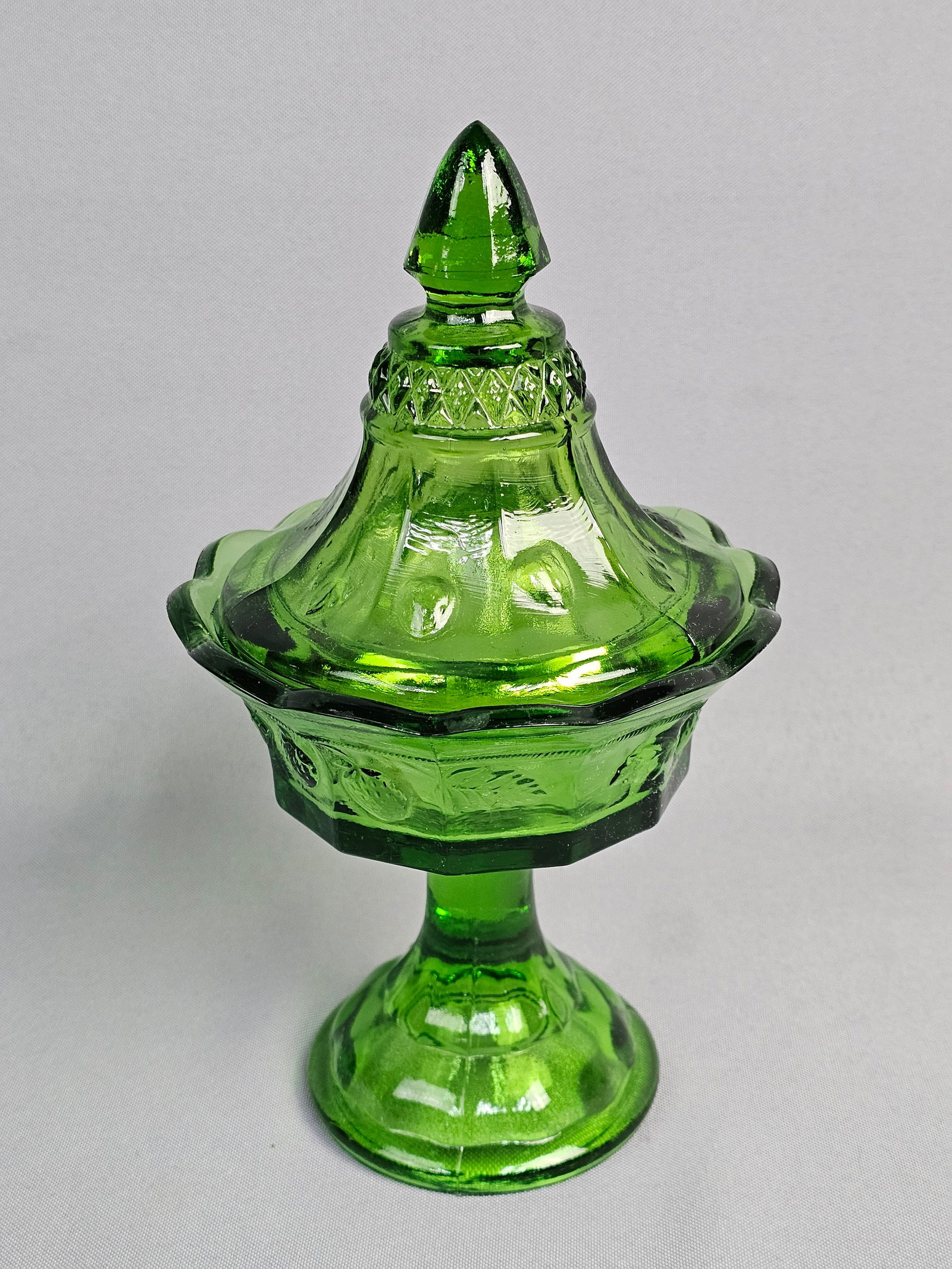 Imperial Glass Emerald Green Harvest Pattern Covered Candy Dish: A vintage emerald green pressed glass covered compote manufactured by the Imperial Glass Corporation. The piece features a multi-paneled body decorated with molded fruit motifs including strawberries,