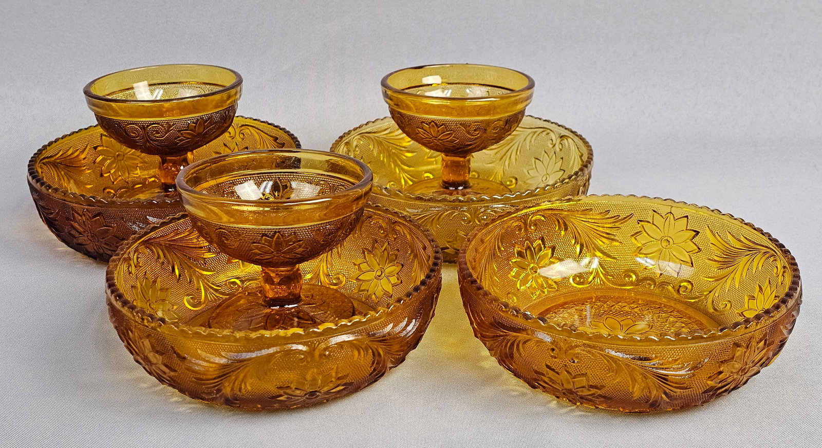 A Set of Amber Pressed Glass Bowls and Footed Cups in the Sandwich Pattern Attributed to Indiana Gla: A set of amber-colored pressed glass tableware in the Sandwich pattern, attributed to Indiana Glass. This collection consists of several small bowls and footed dessert cups. Bowls: 6 inches diameter,