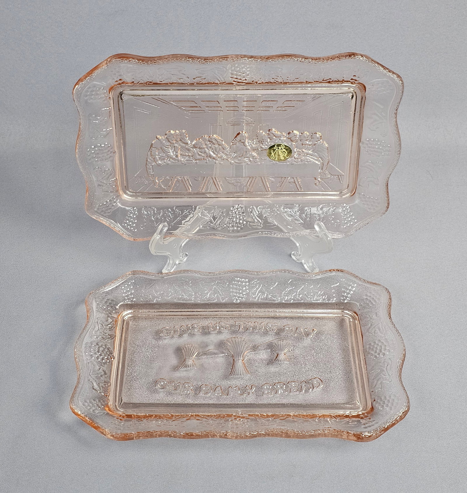 A Pair of Tiara Exclusives Pink Pressed Glass Commemorative Trays: A pair of rectangular pink pressed glass trays marketed by Tiara Exclusives. The first tray features a central panel with a high-relief molded depiction of Leonardo da Vinci's The Last Supper. The sec
