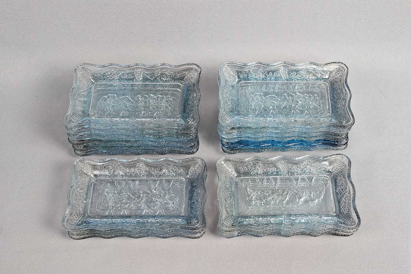 A Set of Eighteen Tiara Exclusives Miniature Pressed Glass Lords Supper Plates: This lot consists of eighteen miniature rectangular plates produced for Tiara Exclusives. Each plate is constructed from light blue transparent pressed glass and features a central bas-relief depictio