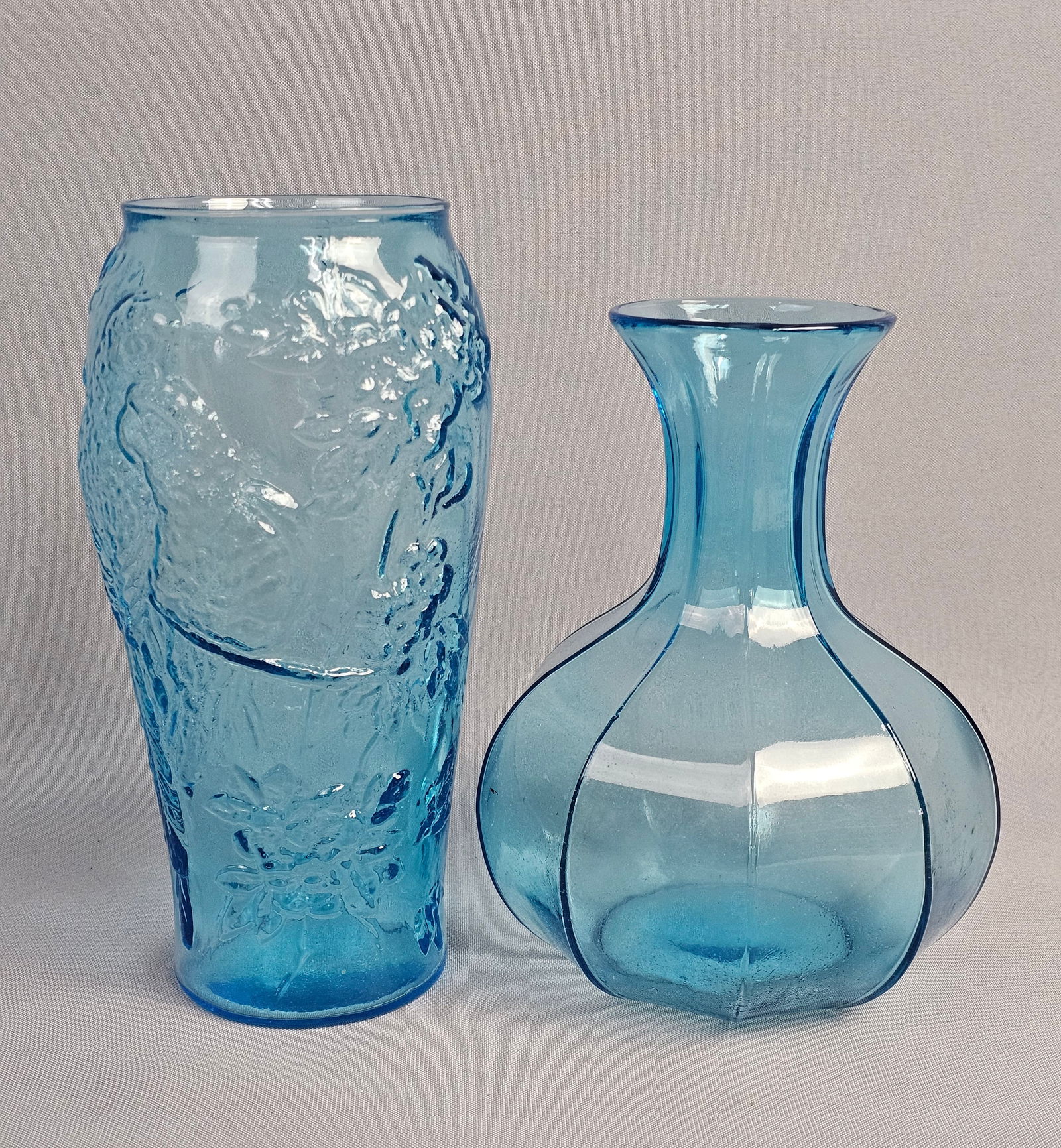 Two Tiara Exclusives Blue Pressed Glass Vases: This lot features two blue pressed glass vases. Neither item shows visible maker marks or signatures. Vases measure 8 and 9 inches tall. Both items are in good condition with no visible chips, cracks,