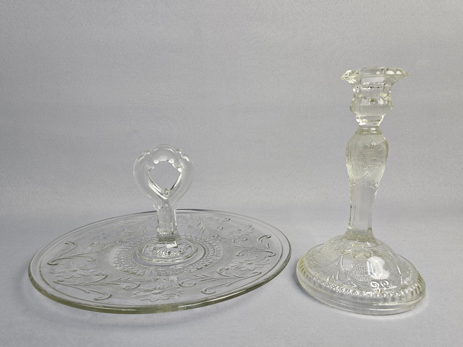 Indiana Glass Clear Handled Server and Candlestick: This lot features two pieces of clear pressed glass in the Sandwich pattern, produced by the Indiana Glass Company and distributed by Tiara Exclusives. The collection includes a center-handled server