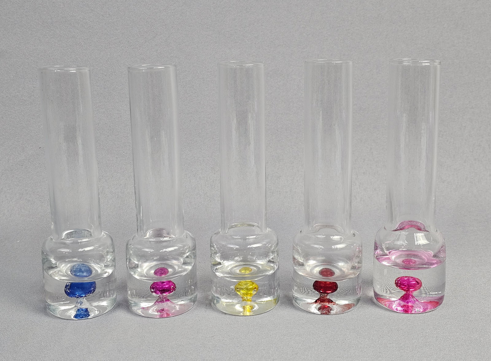 A Set of Five Hand Blown Glass Bud Vases with Sommerso Bases: This collection consists of five hand-blown clear glass bud vases. Each vessel is constructed with a tall, slender cylindrical neck and a weighted, solid clear glass base. The base of each vase featur