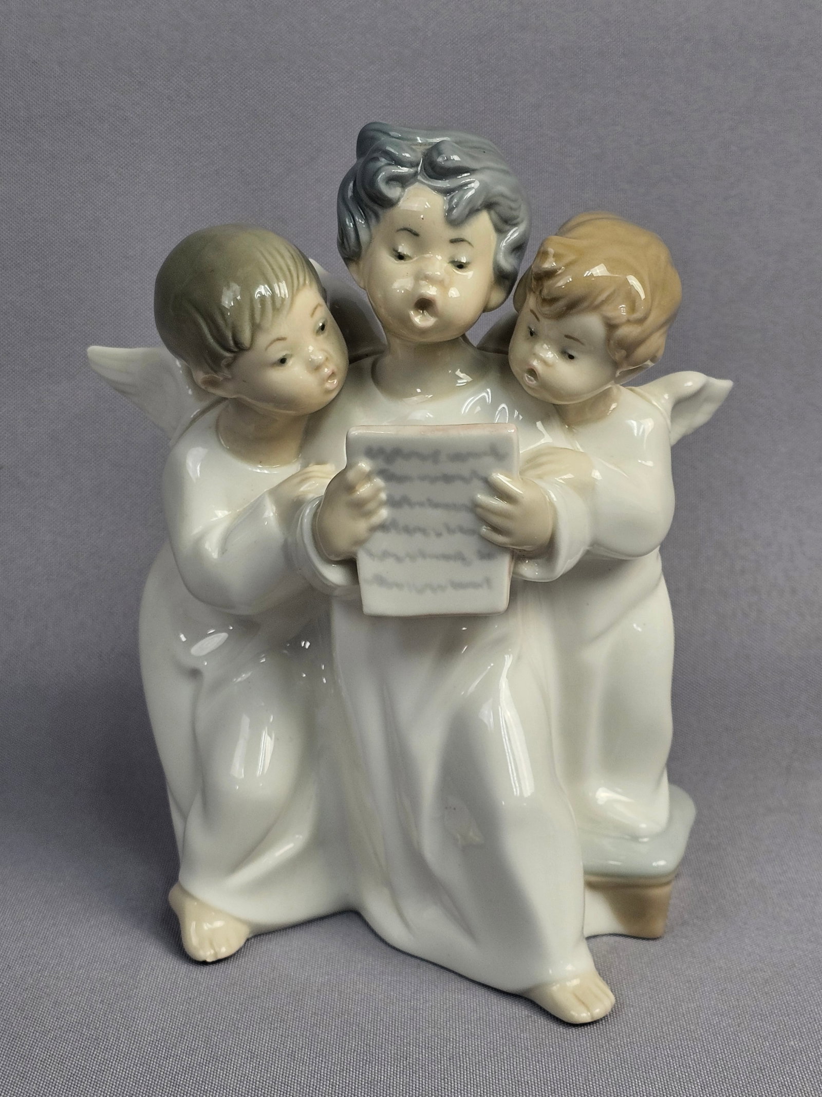 Lladro Angels Group Glazed Porcelain Figurine Model 4542: This Lladro porcelain figurine, titled Angels Group (model number 4542), depicts a trio of winged cherubs huddled together while singing from a single sheet of music. The piece is executed in a high-g