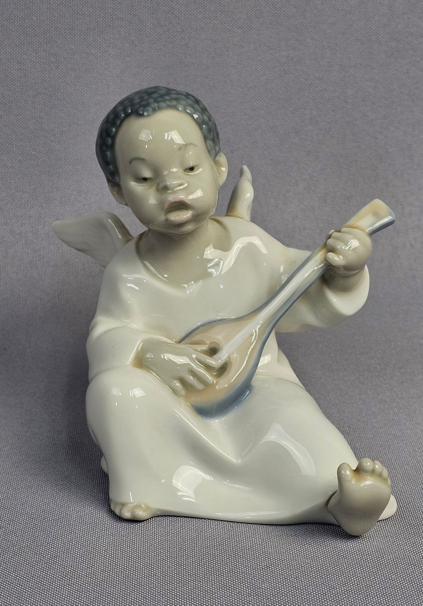 Lladro Angel with Mandolin Black Figurine Model 4537: A glazed porcelain figurine produced by Lladro, identified as the Angel with Mandolin (Black), model number 4537. The piece depicts a seated winged cherub with African features and textured hair, show