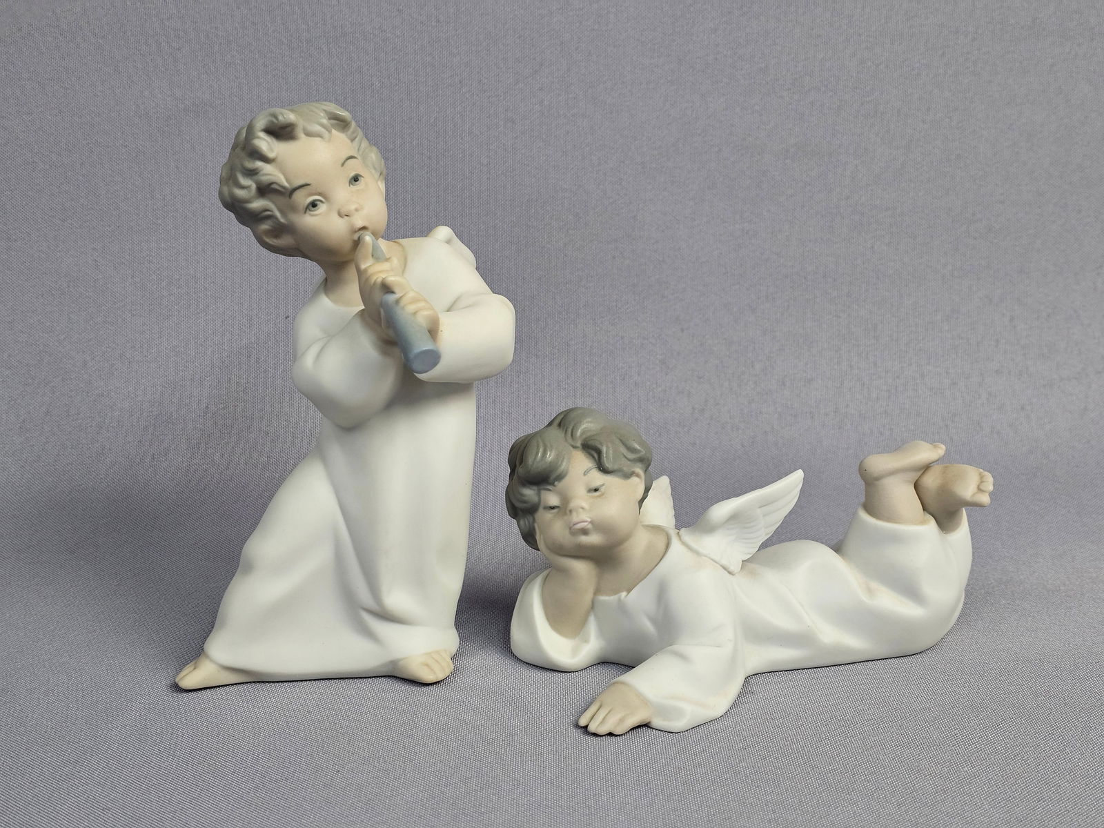 A Pair of Lladro Matte Porcelain Angel Figurines: A pair of Lladro porcelain figurines featuring two angels in a matte bisque finish. The first figurine is identified as Angel with Flute, model 4540, depicting a kneeling winged figure in a long robe
