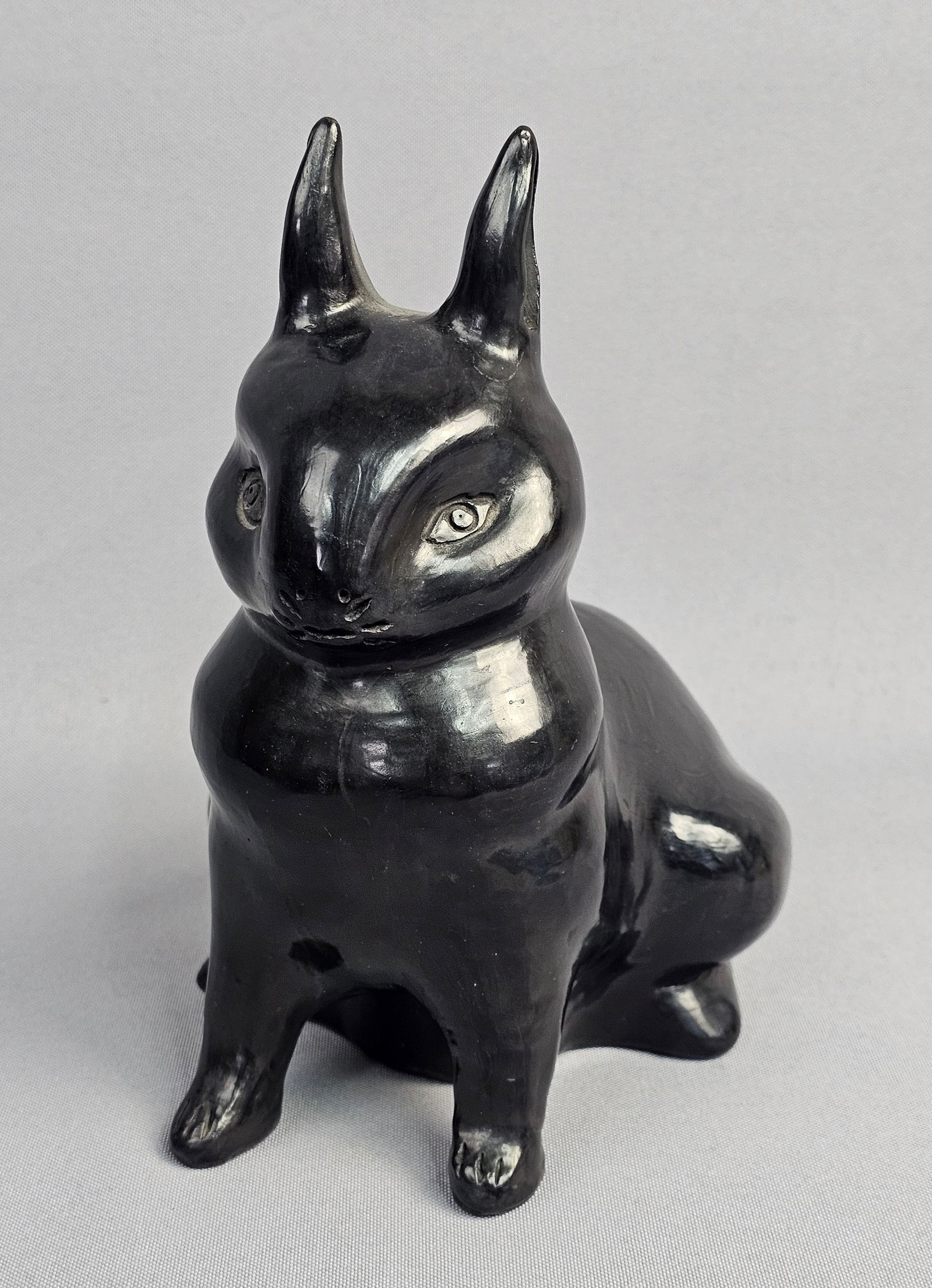 Mexican Barro Negro Ceramic Sitting Rabbit Figurine Alfareria Dona Rosa: This ceramic figurine depicts a stylized sitting rabbit crafted from Barro Negro, or black clay, from San Bartolo Coyotepec, Oaxaca, Mexico. The piece is attributed to Alfareria Dona Rosa, the