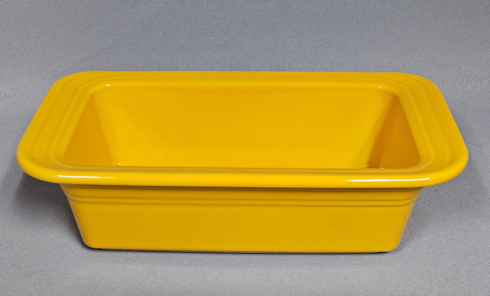 Fiesta Sunflower Yellow Ceramic Loaf Pan: A Fiesta ceramic loaf pan manufactured by the Homer Laughlin China Company. This rectangular baking dish is finished in a solid sunflower yellow glaze. The piece features the signature molded