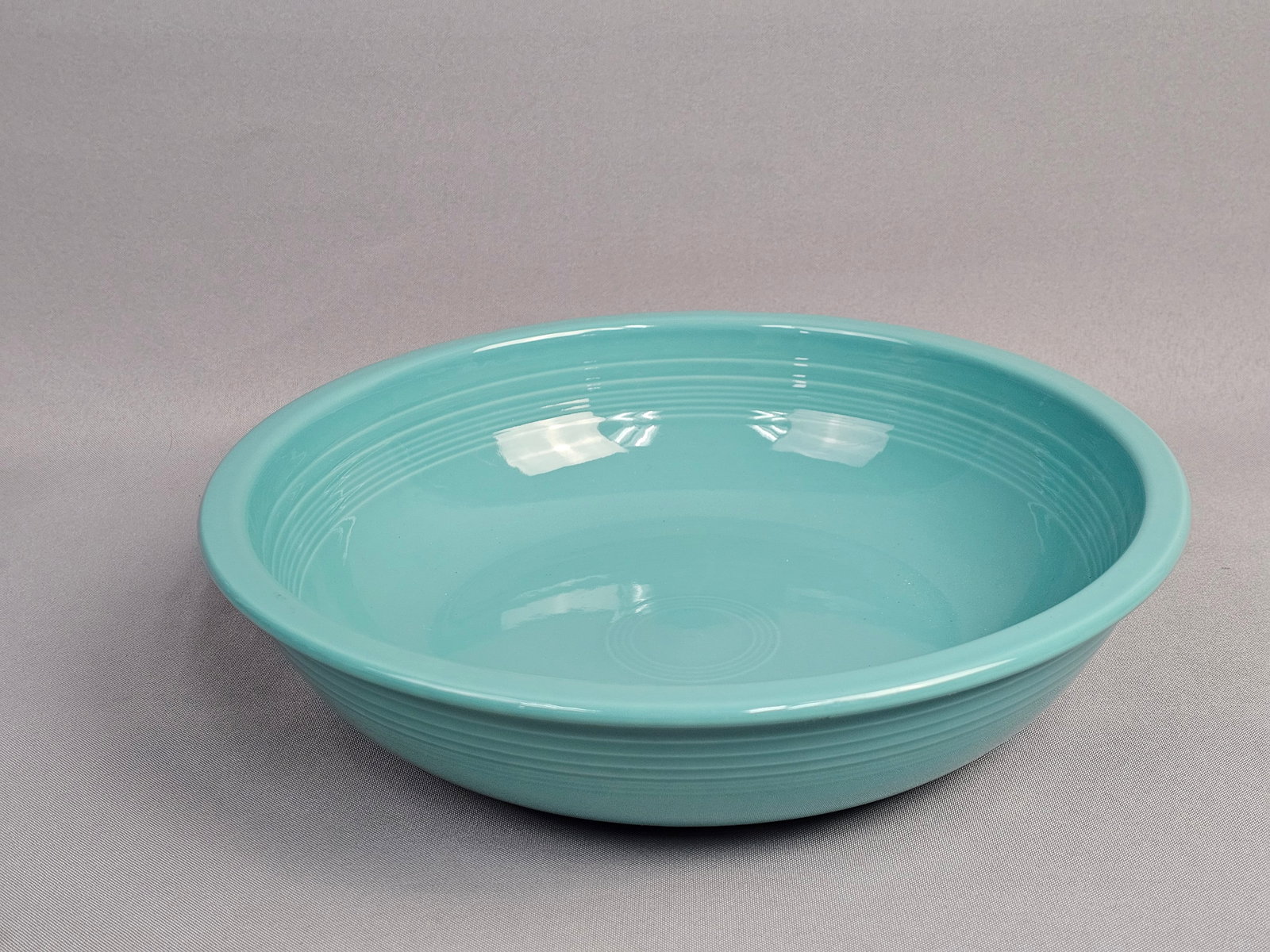 Homer Laughlin Fiesta Turquoise Large Serving Bowl: A large round serving bowl from the Fiesta product line manufactured by the Homer Laughlin China Company. The bowl is constructed from vitrified ceramic and finished in a solid turquoise glaze. It
