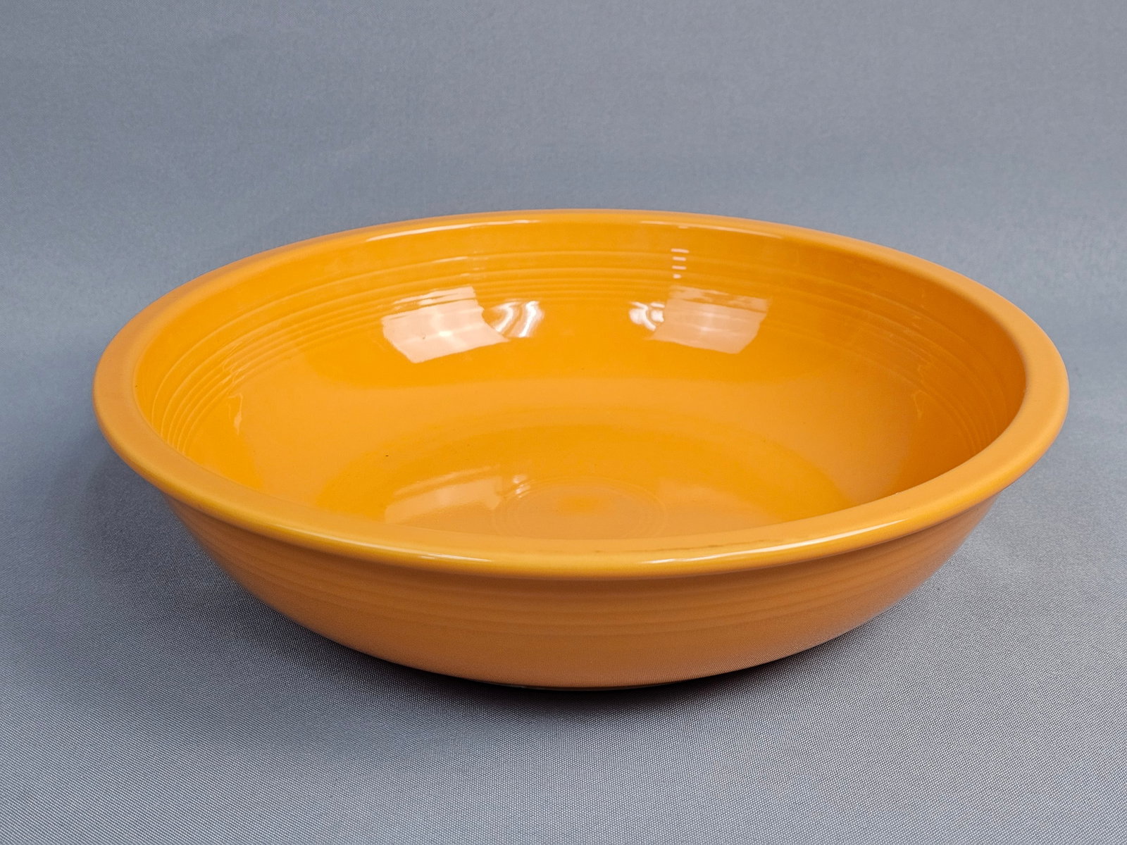 Homer Laughlin Fiesta Tangerine Orange Bistro Serving Bowl: A glazed vitreous china serving bowl from the Fiesta line by the Homer Laughlin China Company. The bowl features a deep, round form with a flared rim and is finished in a solid tangerine orange glaze.
