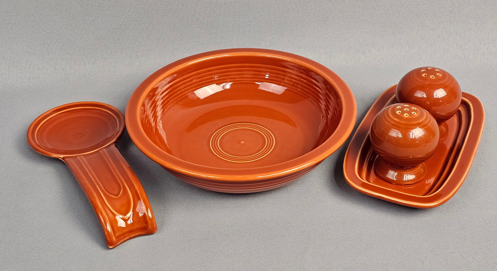 A Group of Fiesta Red Glazed Earthenware Kitchenware: This collection of glazed earthenware is produced by the Homer Laughlin China Company as part of the Fiesta line. The pieces are finished in a vibrant, high-gloss orange-red glaze and feature the
