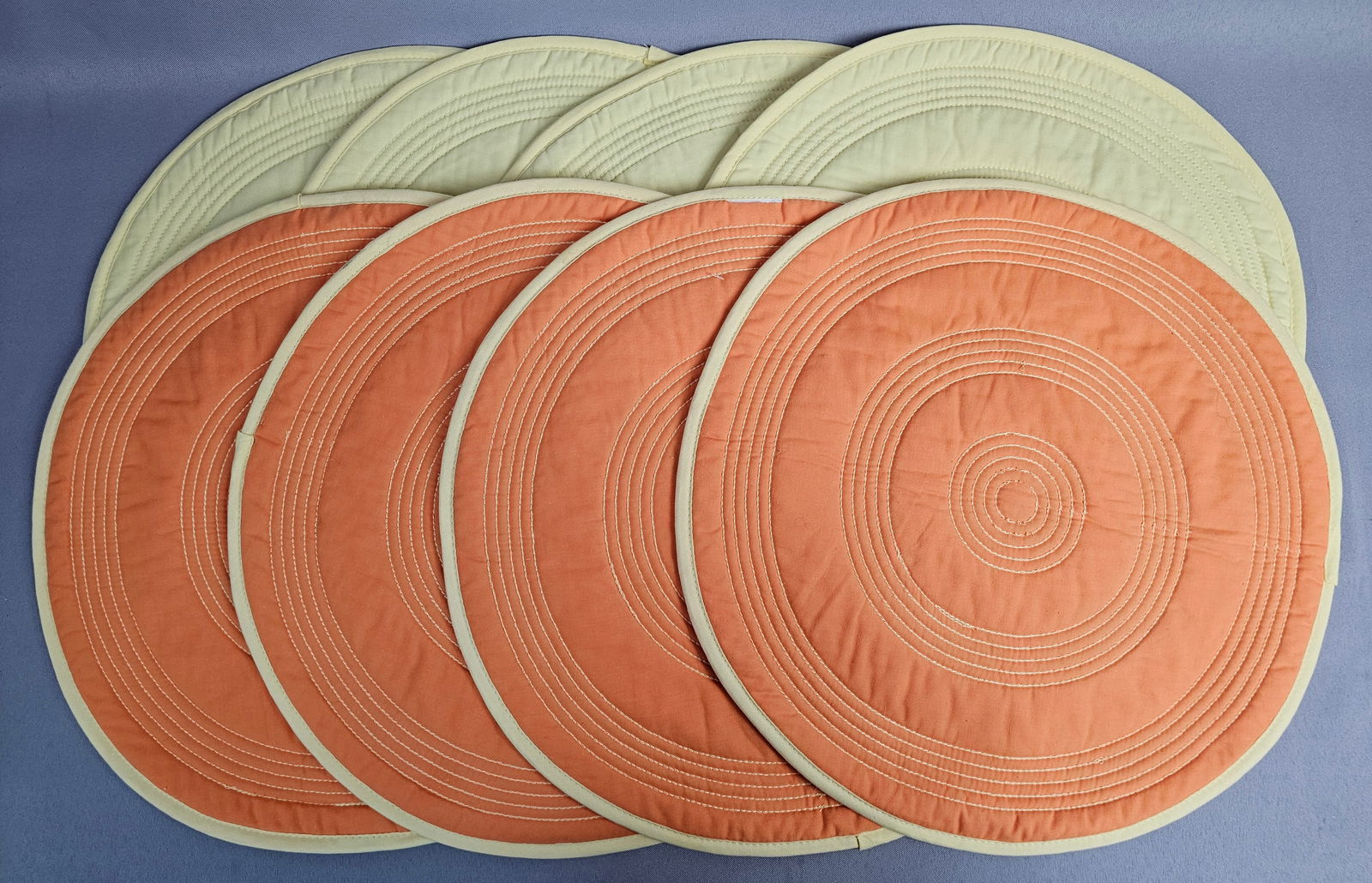Set of Eight Fiesta Reversible Quilted Circular Placemats: A set of eight reversible circular quilted placemats manufactured by The Homer Laughlin China Co. under the Fiesta brand. These textiles are constructed from a quilted fabric featuring machine-sewn co