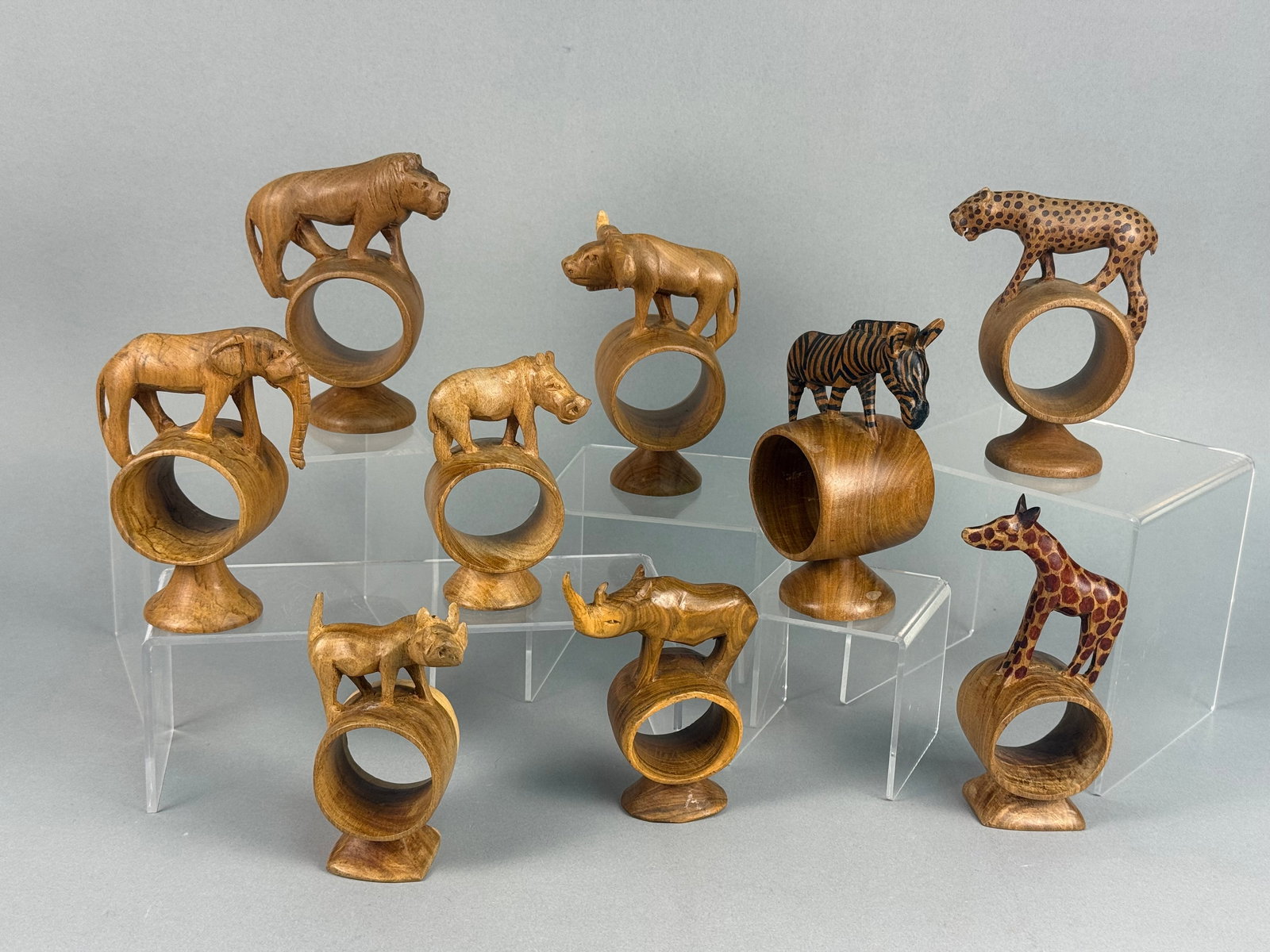 A Collection of Hand-Carved African Safari Animal Wooden Napkin Rings: A collection of hand-carved wooden napkin rings, each featuring a different African safari animal figure including a lion, elephant, rhinoceros, giraffe, zebra, Cape buffalo, cheetah, hippopotamus, an