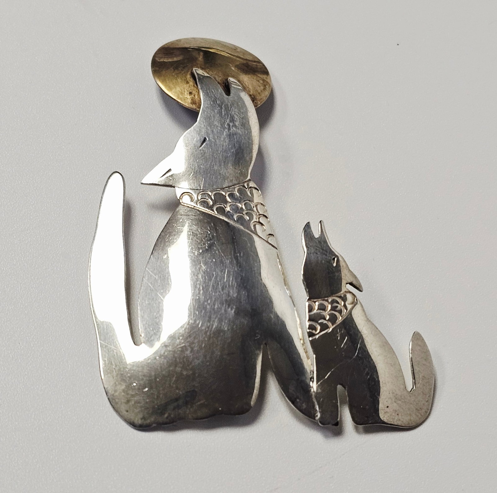 Southwestern Sterling Howling Wolf Brooch 10.5 Grams: A contemporary Southwestern style brooch depicting two howling wolves positioned beneath a circular moon element. The wolves are crafted from polished sterling silver while the moon is composed of a c