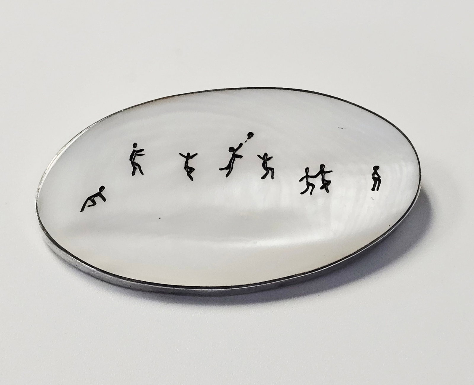 Sterling and Mother-of-Pearl Figural Brooch 26.9 Grams: This oval brooch features a panel of mother-of-pearl set within a sterling silver frame. The panel is held in a bezel setting with a closed back. The reverse features a horizontal pin with a rotating