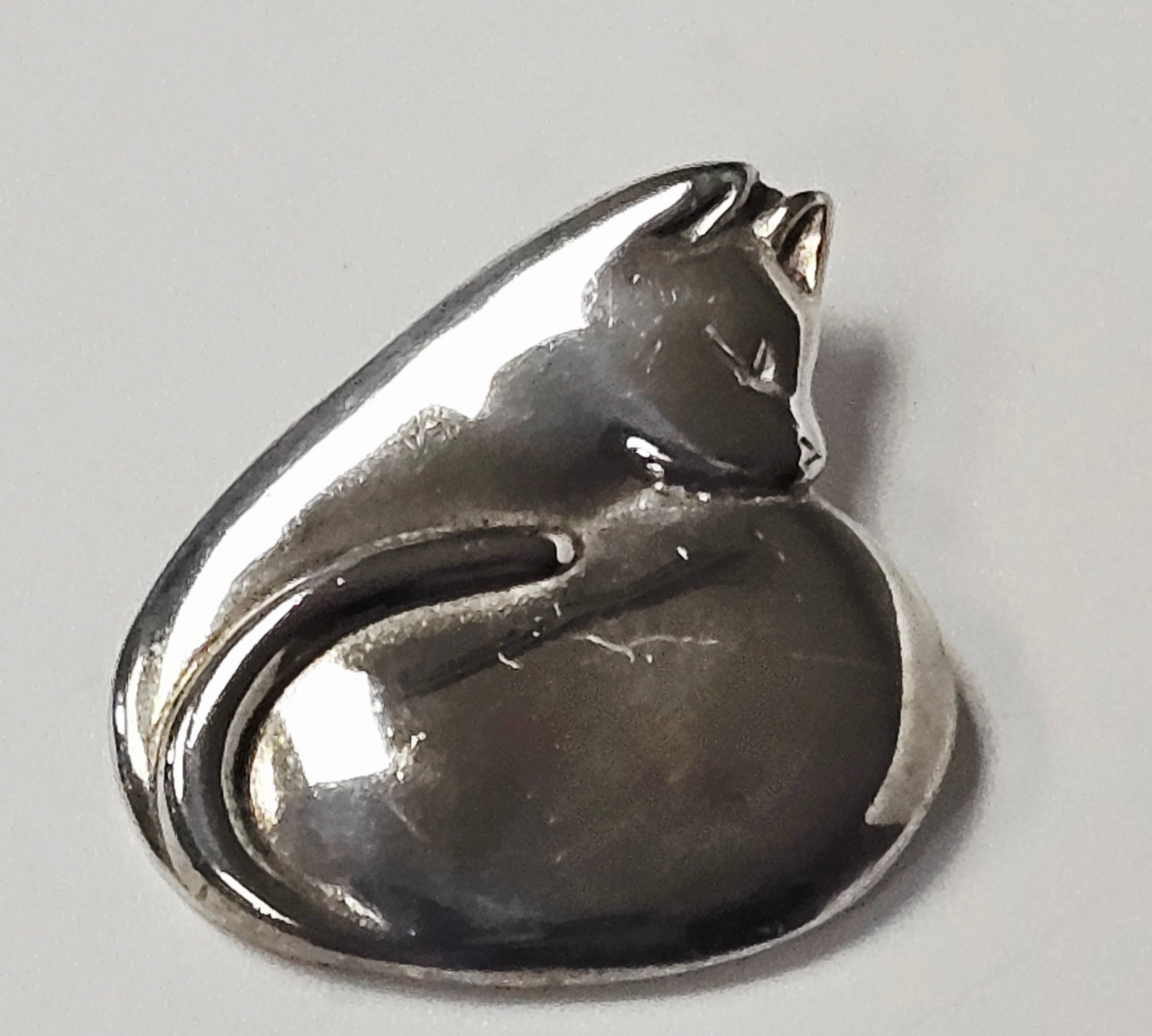 H&H deMatteo Modernist Sterling Cat Brooch 11.8 Grams: This modernist brooch is designed in the form of a stylized, curled sleeping cat. The piece features an organic, rounded shape with a high-polish finish. Minimalist recessed lines are used to define