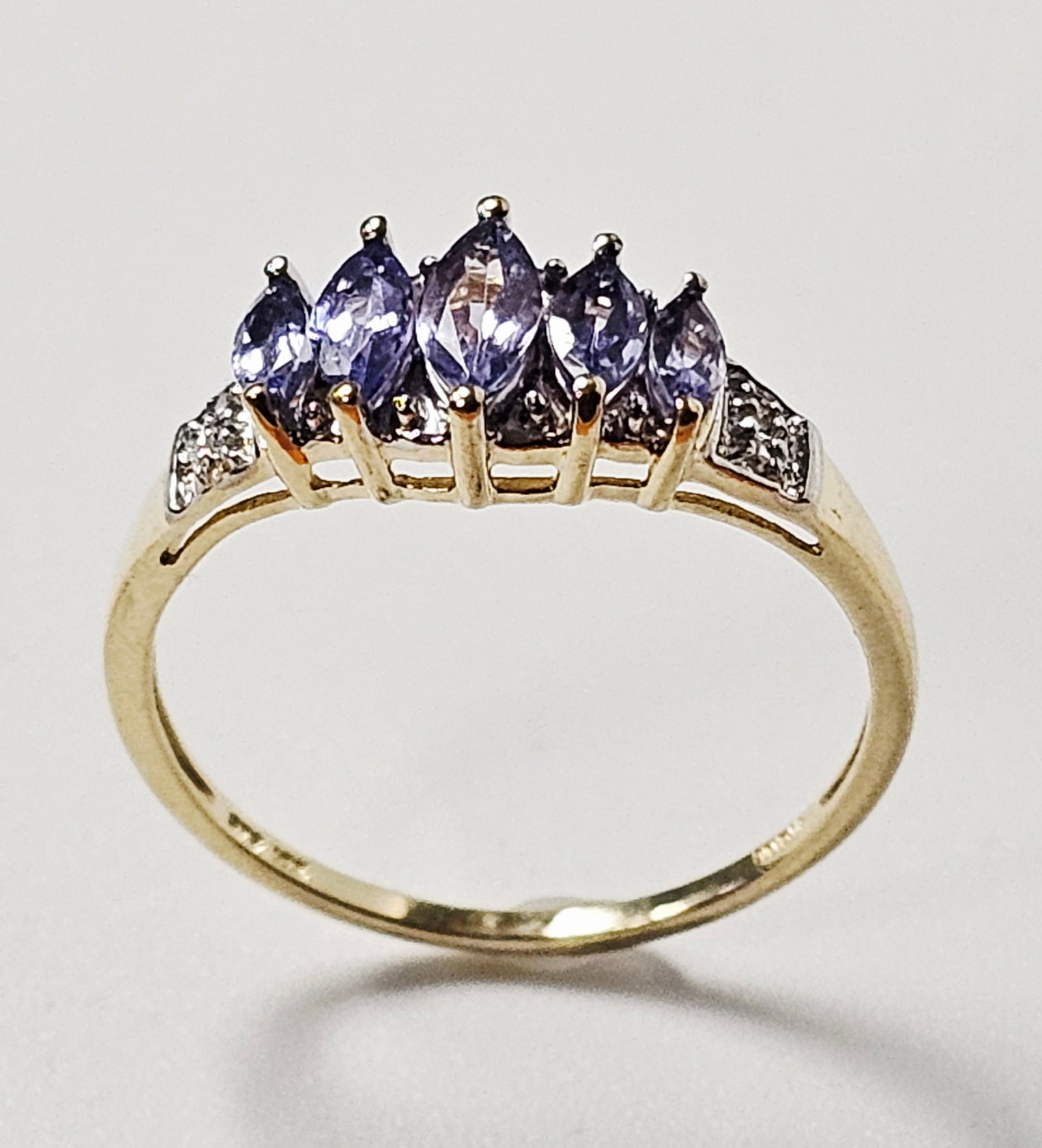 10K Gold Tanzanite & Diamond Ring 1.7 Grams: A 10 karat yellow gold fashion ring featuring five graduated marquise-cut violet-blue tanzanite, in a shared-prong setting. The central row is flanked by tapered shoulders containing small round-cut