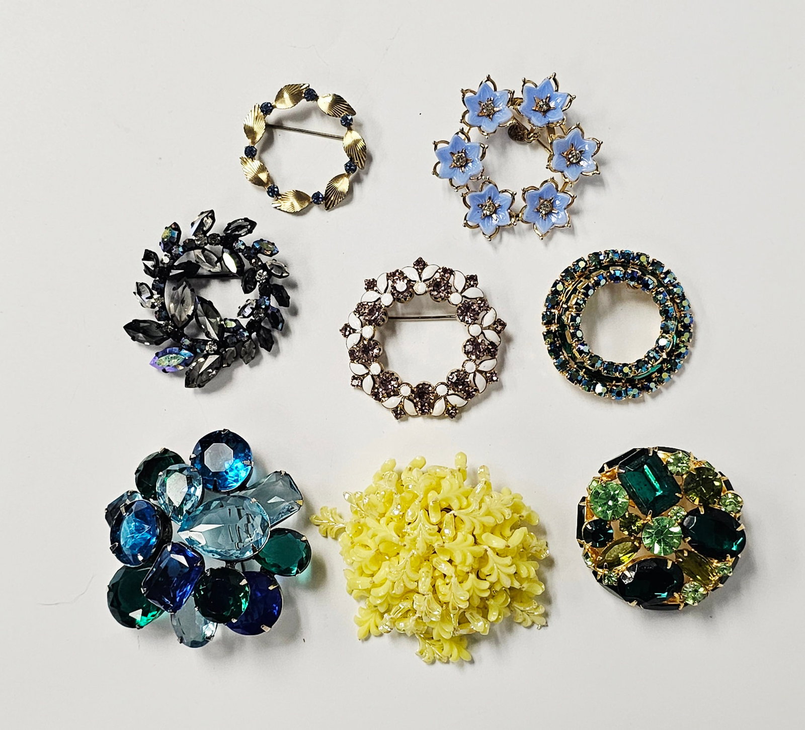 A Collection of Eight Vintage Costume Jewelry Brooches: This collection consists of eight vintage costume jewelry brooches featuring various floral, wreath, and cluster designs. The group includes several marked pieces: a black-tone wreath brooch with