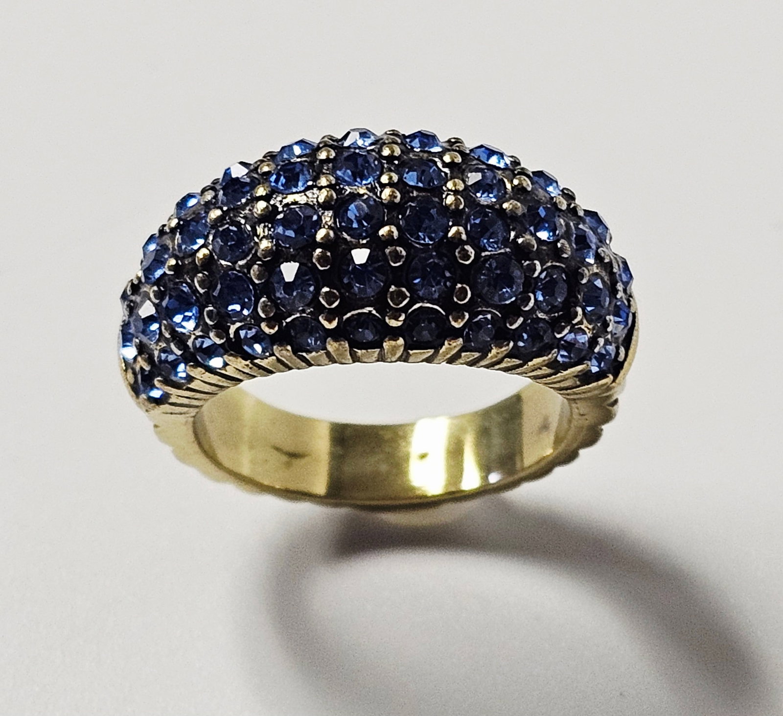 Heidi Daus Blue Crystal Cocktail Ring: A dome-style cocktail ring by designer Heidi Daus. The piece is constructed from antiqued gold-tone metal and features a high-domed top encrusted with multiple rows of pave-set, faceted blue