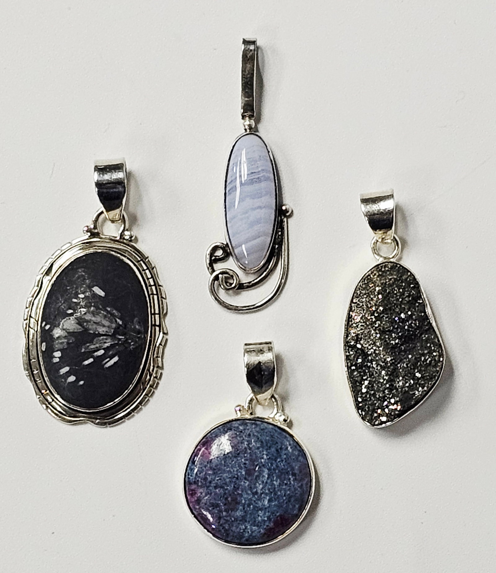 Four Sterling Silver & Natural Stone Pendants 23.4 Grams: A collection of four pendants featuring various natural stones set in sterling silver. The first item is an oval cabochon of what appears to be snowflake obsidian, featuring a black matrix with white