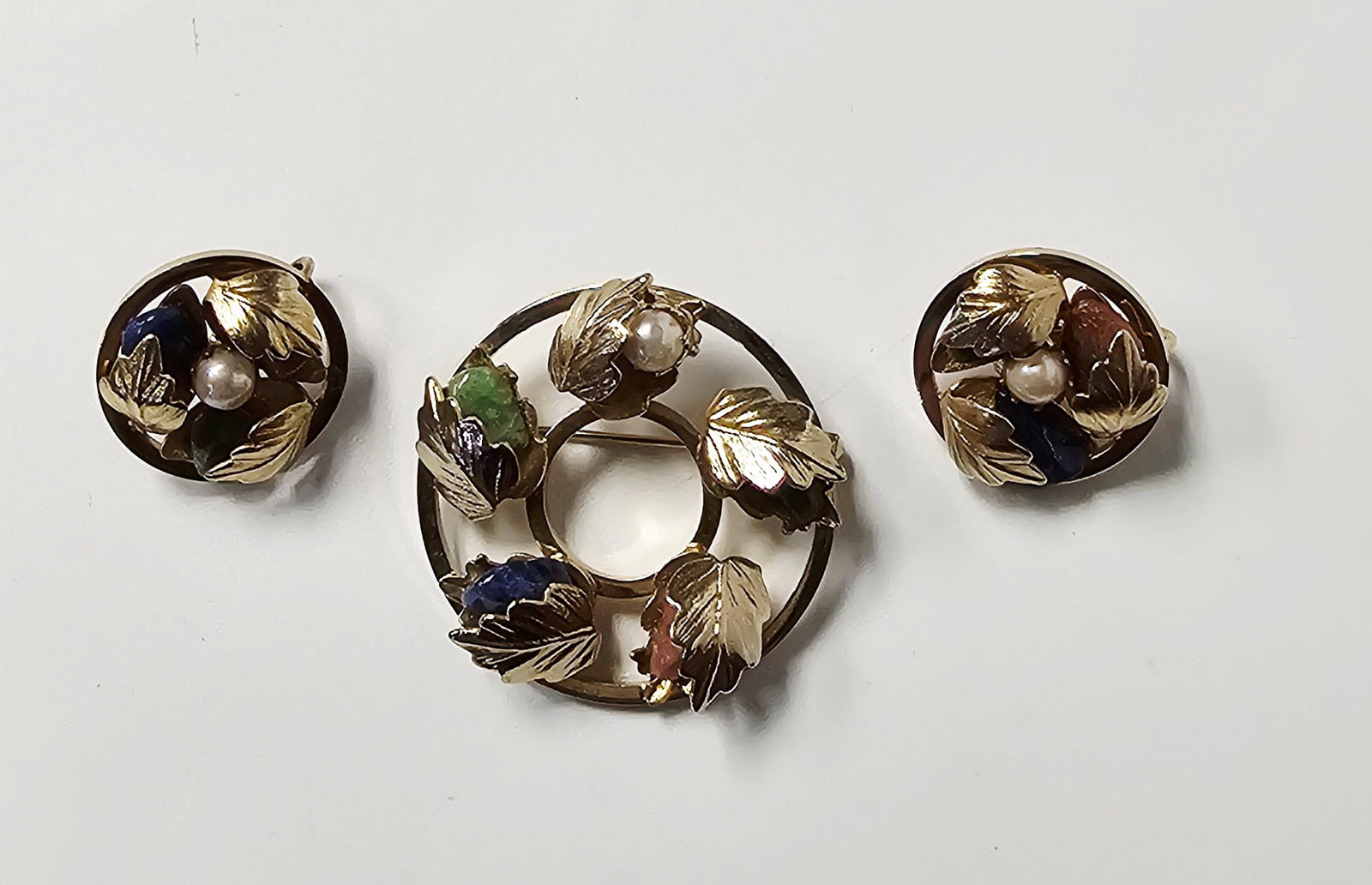 Sarah Coventry Stone Leaf Motif Brooch & Earrings: This Sarah Coventry costume jewelry collection consists of a circular wreath brooch and a matching pair of clip-on earrings. The pieces are constructed from yellow-toned base metal featuring a texture