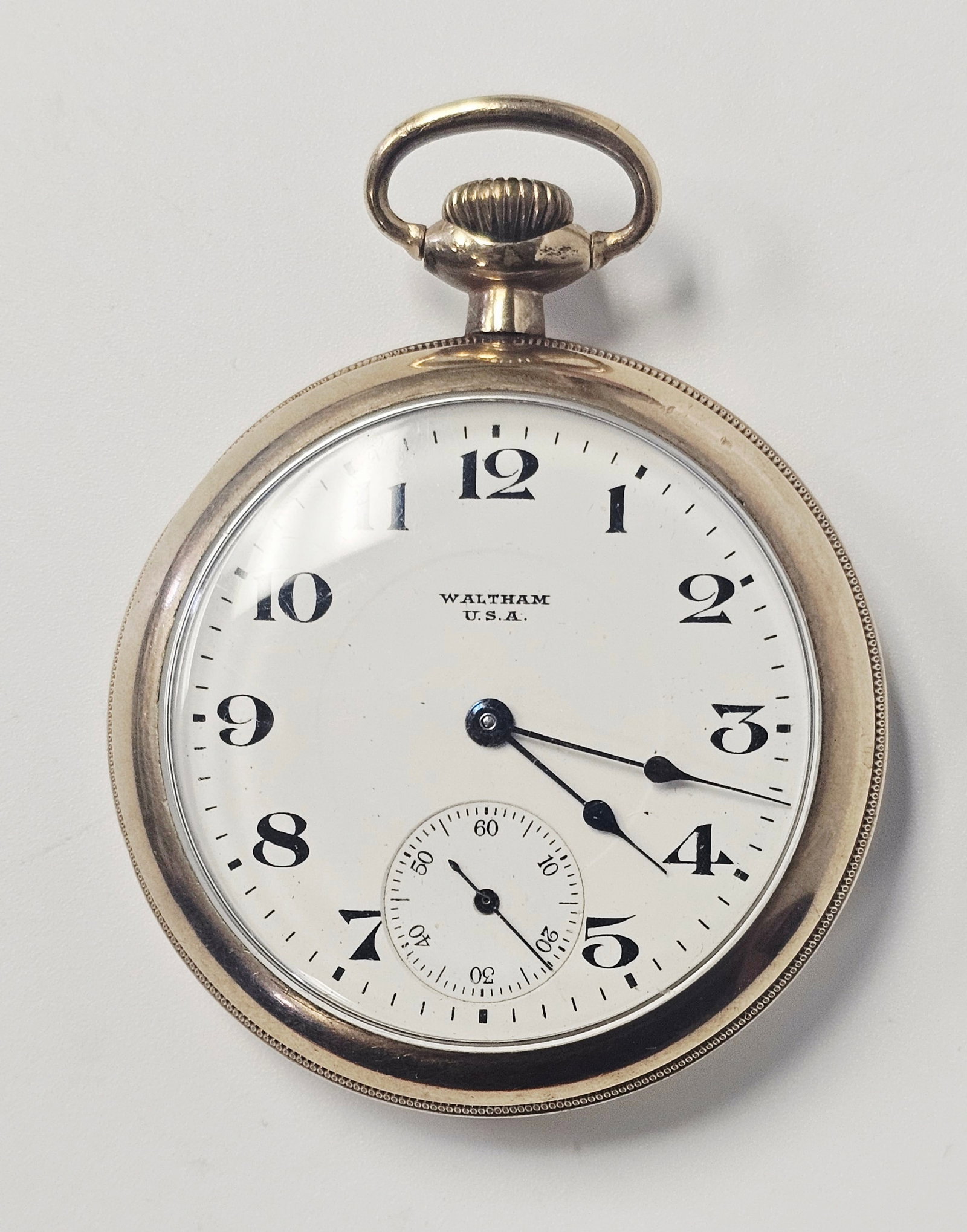 Waltham 17 Jewel Gold Filled Open Face Pocket Watch: This open-face pocket watch features a white dial with black Arabic numeral hour markers, a subsidiary seconds dial at the 6 o'clock position, and blued steel hands. The dial is marked Waltham U.S.A.