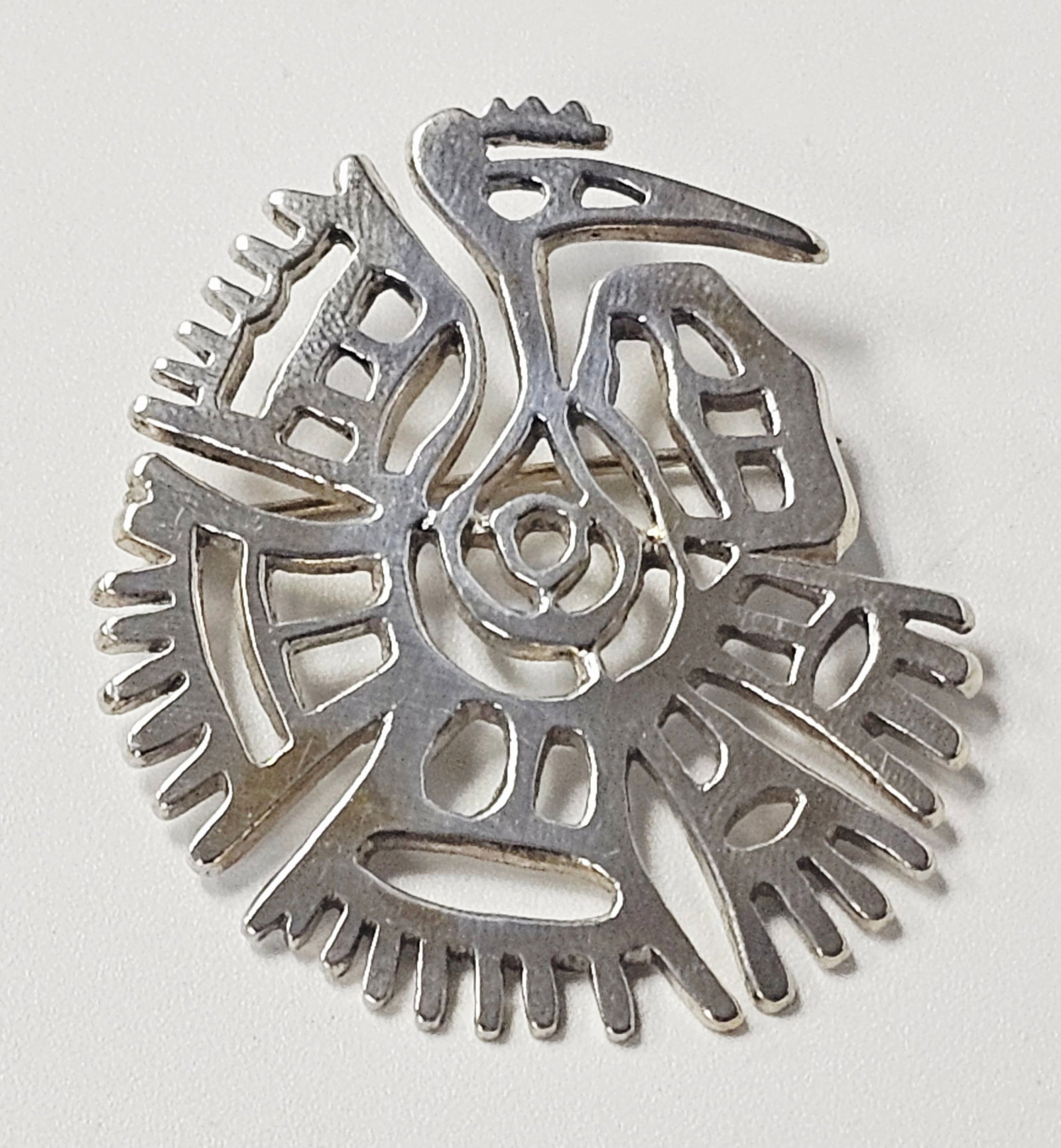 Mexican Sterling Bird Brooch by MBS 12.9 Grams: A sterling silver brooch of circular form featuring a stylized, openwork avian design. The geometric composition includes a central bird head with a large beak, surrounded by radiating pierced element