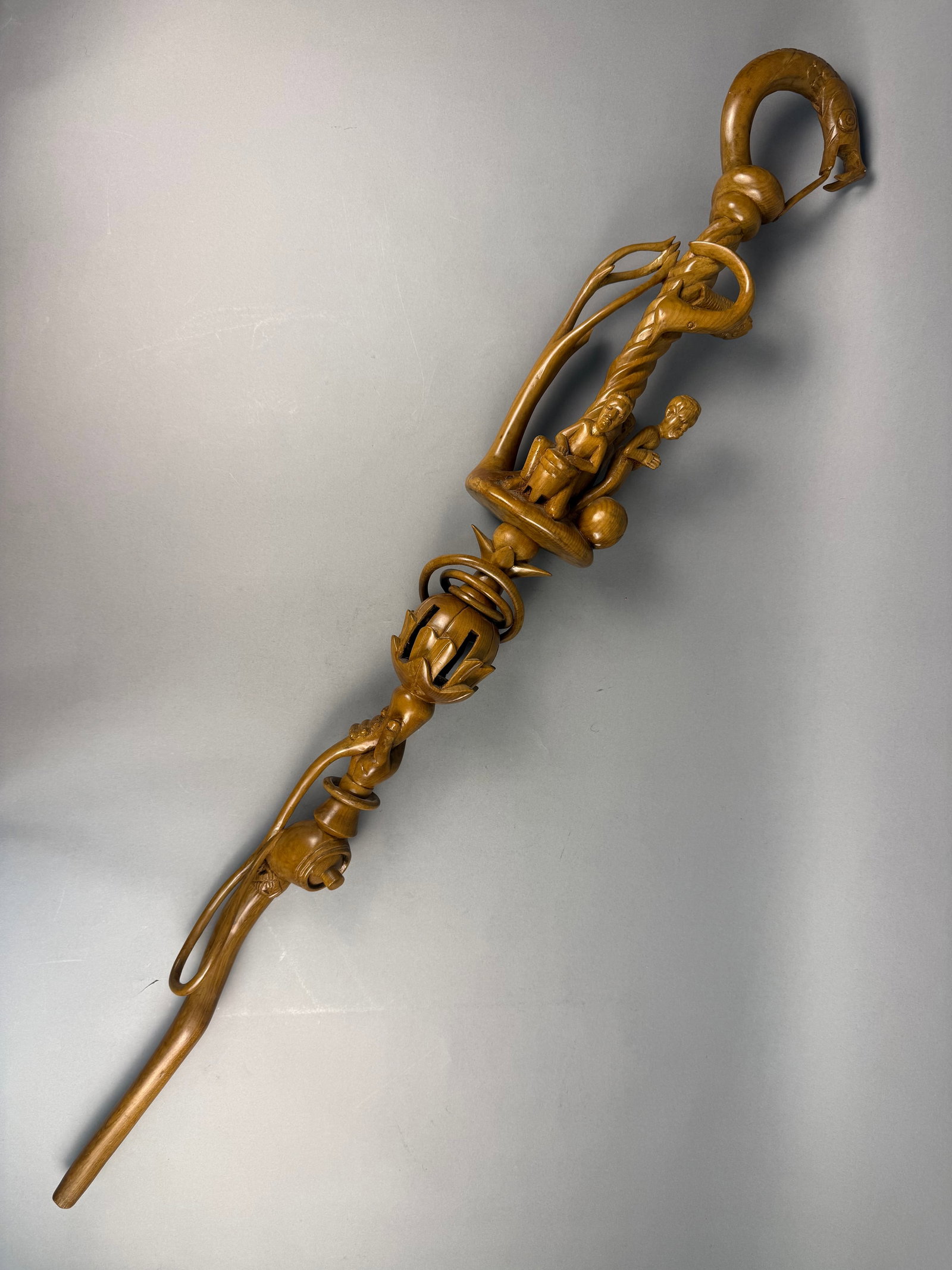 Hand Carved Hardwood African Nyami Nyami Style Staff: A hand-carved brown wooden staff featuring figurative elements including human forms, fish, a gripping hand, free floating rings and a ball in a cage. measuring approximately 43 inches in length. ov