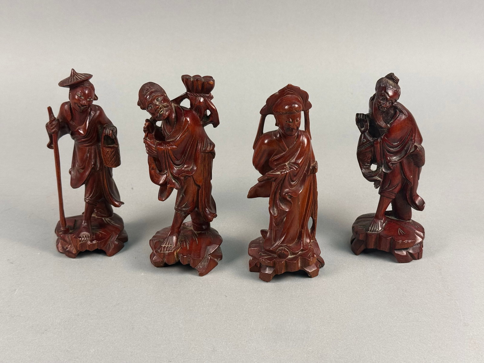 A Set of Four Chinese Carved Boxwood Figurines: This set of four hand-carved figurines is crafted from wood, likely boxwood, featuring a polished reddish-brown stain. The collection depicts traditional Chinese characters, possibly representing folk