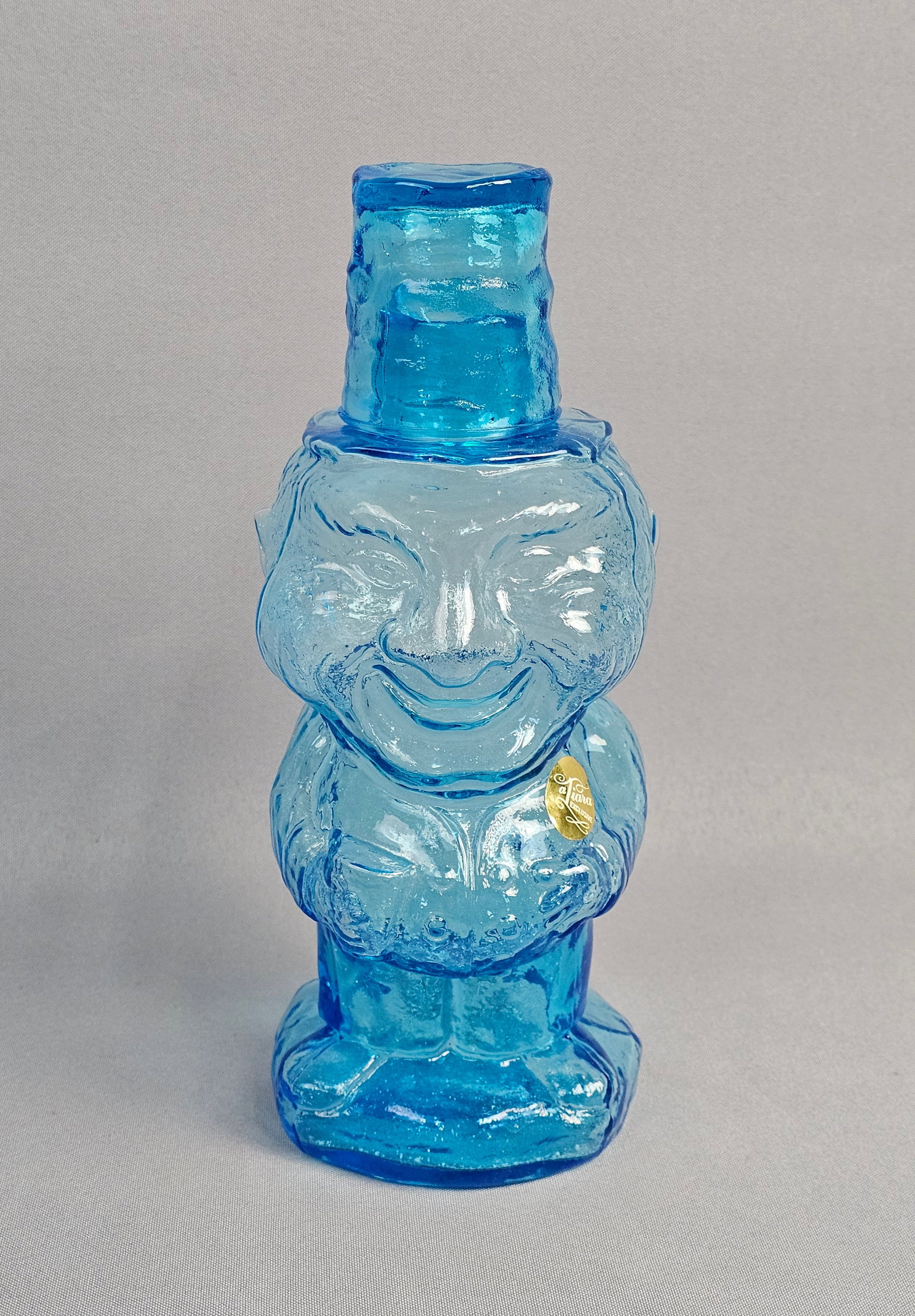Tiara Exclusives Blue Glass Jolly Mountaineer Figural Decanter: This figural decanter, identified as the Jolly Mountaineer pattern, was distributed by Tiara Exclusives and manufactured by the Indiana Glass Company. The item is made of heavy pressed glass in a