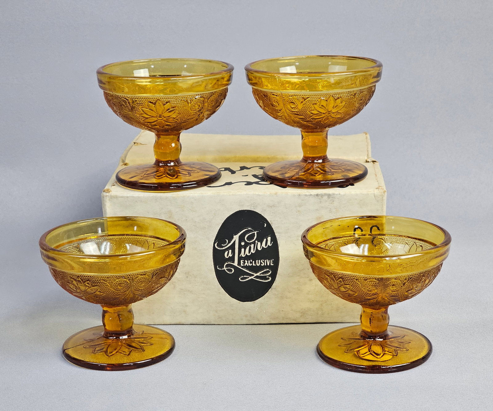 A Set of Tiara Exclusives Amber Sandwich Pattern Pressed Glass Sherbet Cups: This set of footed sherbet or dessert cups is produced in the Sandwich pattern by Tiara Exclusives. The glassware is constructed of transparent amber pressed glass. Height: 3 inches each The glasswa