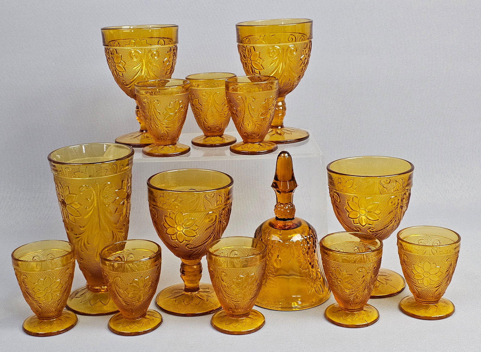 Fourteen Assorted Pieces of Indiana Glass Tiara Amber Sandwich Pattern Tableware: This collection consists of pieces of amber-colored pressed glass tableware in the Sandwich pattern, attributed to the Indiana Glass Company for Tiara Exclusives. The glassware features a floral and s