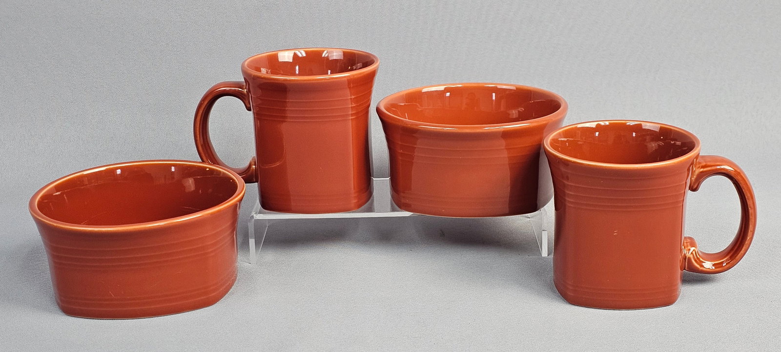 A Collection of Fiesta Paprika Glazed Ceramic Tapered Mugs and Bowls: This collection of glazed earthenware consists of pieces from the Fiesta line manufactured by the Homer Laughlin China Company in the United States. The items are finished in a reddish-brown color. 