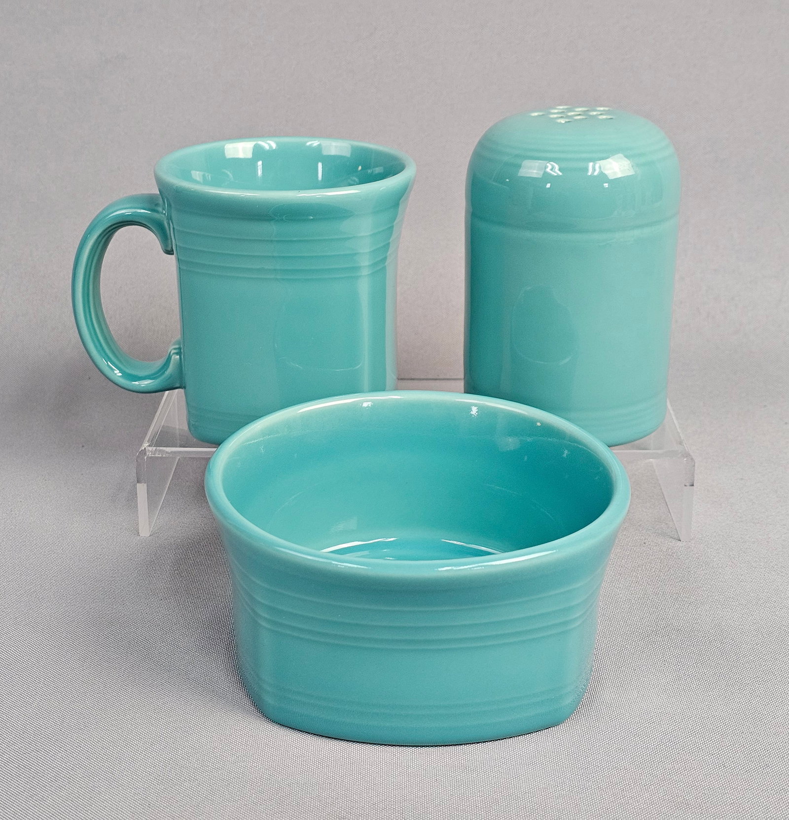 A Trio of Fiesta Turquoise Ceramic Tableware Items: This group of three contemporary ceramic items is from the Fiesta line produced by the Homer Laughlin China Company. The collection consists of a stackable mug, a small deep bowl, and a large