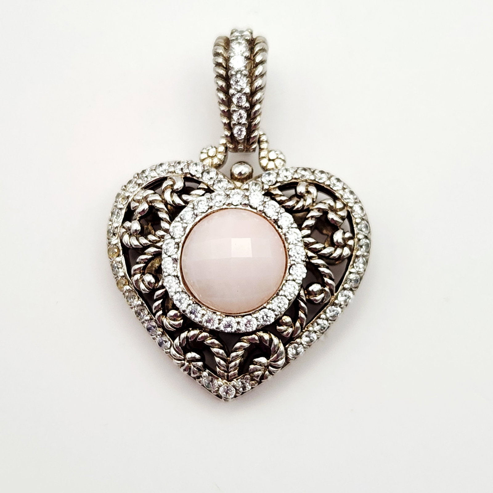 Judith Ripka Sterling Enhancer Pendant 13.9 Grams: A sterling silver heart shaped enhancer pendant by designer Judith Ripka. The piece features a central round pale pink cabochon gemstone measuring approximately 12mm in diameter. The center stone is s