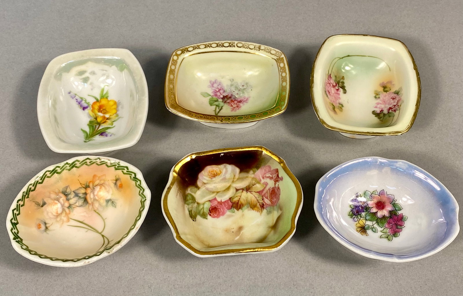 A Set of 6 Vintage and Antique Porcelain Salt Cellars and Nut Dishes: This collection consists of 6 porcelain salt cellars or individual nut dishes in various forms, including rectangular, oval, lobed, and scalloped shapes. The pieces feature a variety of decorative tec