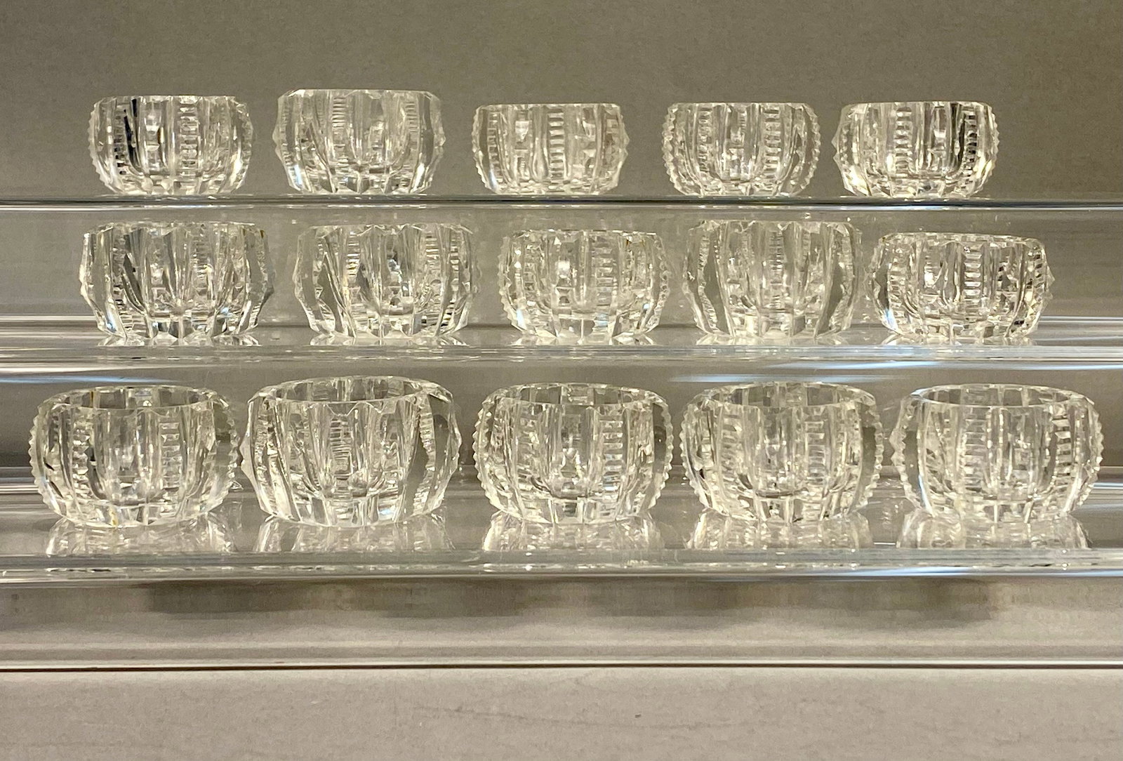 A Set of Fifteen Cut Glass Salt Cellars in a Notched Rib Pattern: This lot consists of a set of fifteen individual clear cut glass open salt cellars. Each piece is crafted from heavy lead crystal, characterized by high clarity and significant light refraction. The f