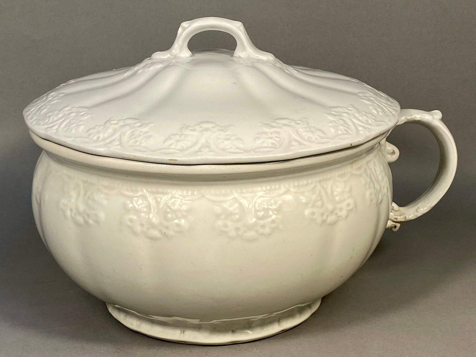 Alfred Meakin Ltd. Royal Ironstone China Lidded Chamber Pot: An English white ironstone lidded chamber pot manufactured by Alfred Meakin Ltd. of Tunstall, Staffordshire. The piece is constructed with a bulbous body and a single large, scrolled handle. The match