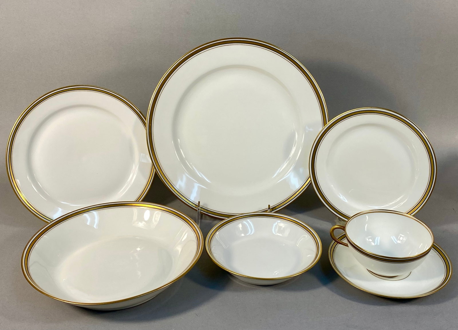 A 35 Piece Set of Old Abbey Limoges Porcelain Dinnerware: This set of fine white porcelain dinnerware is produced by Old Abbey in Limoges, France. Each piece features a bright white ground decorated with a wide, polished gold band at the rim. The gold band i