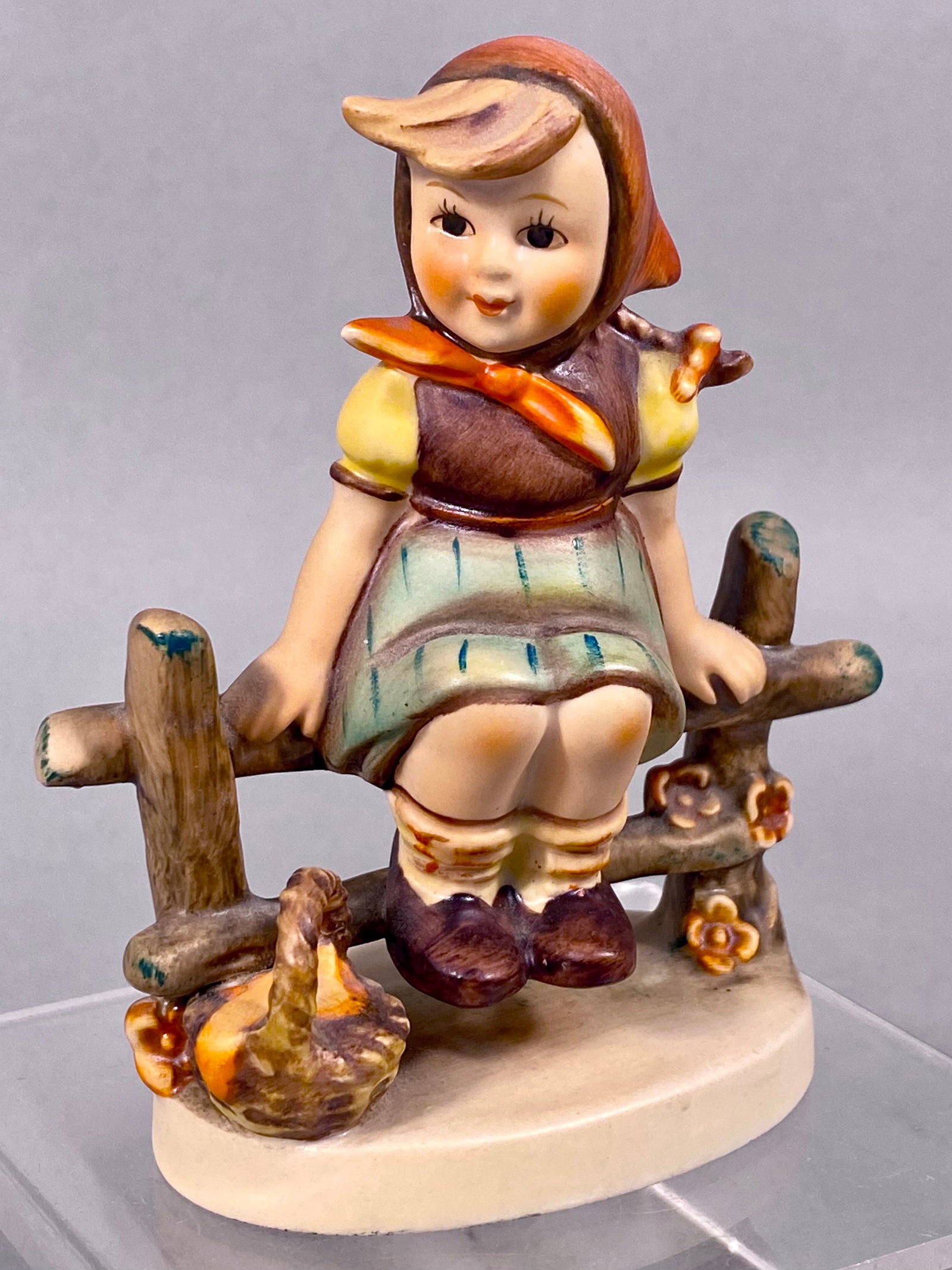 Goebel Hummel Figurine Just Resting 112 3/0 TMK-4: Hand-painted porcelain figurine titled Just Resting, manufactured by Goebel. The figure depicts a young girl in traditional dress seated on a wooden rail fence with a small woven basket at her side. T