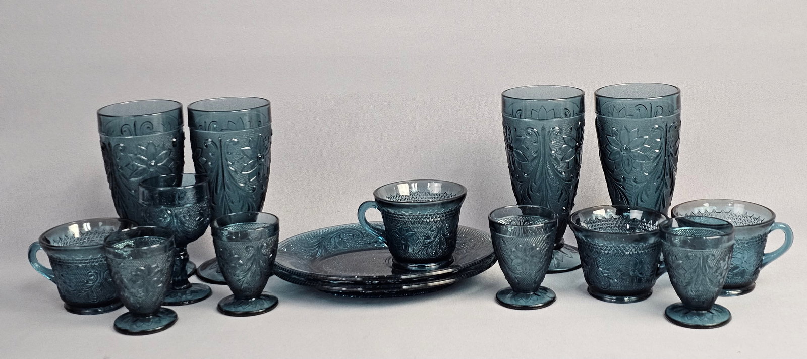 A Collection of Teal Blue Pressed Glass Tableware in the Sandwich Pattern Attributed to Indiana: This collection of fifteen pieces of pressed glass is attributed to the Indiana Glass Company for Tiara Exclusives in the Sandwich pattern. The pattern features intricate molded floral motifs and scro