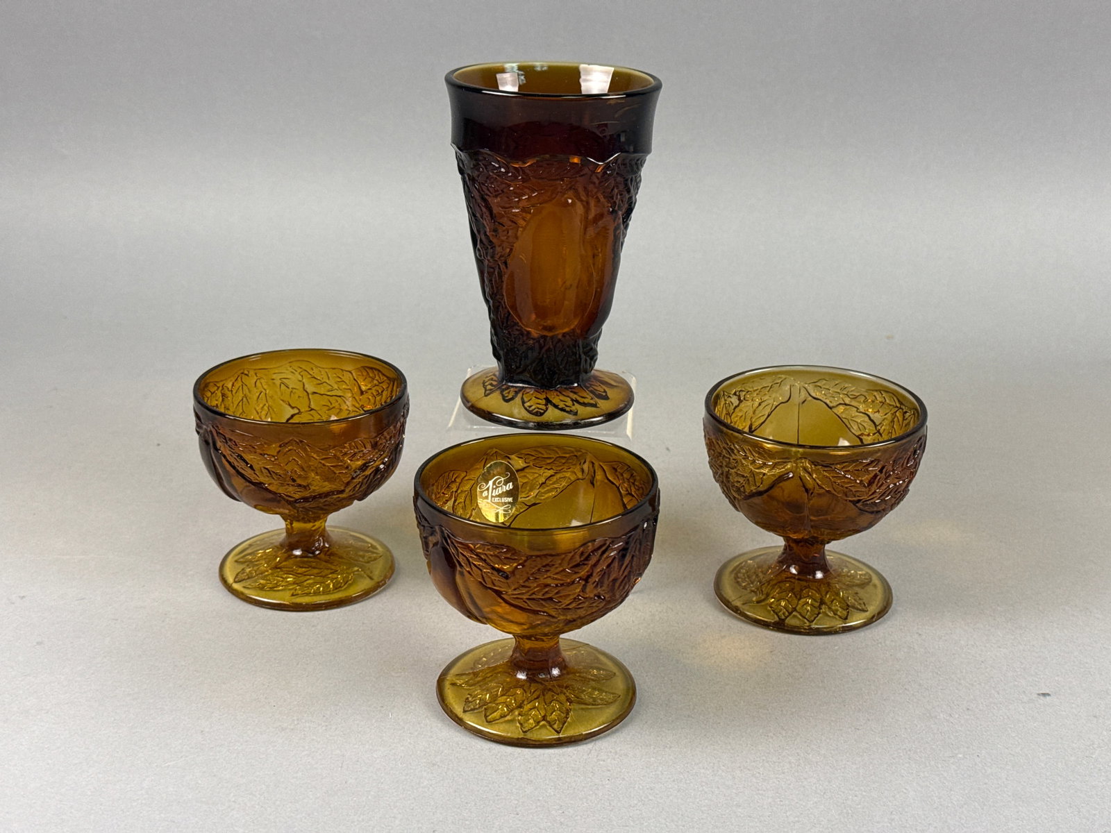 A Set of Four Tiara Exclusives Amber Pears Pattern Glassware Pieces: A set of four amber pressed glass items in the Fruit pattern, distributed by Tiara Exclusives and manufactured by the Indiana Glass Company. The set includes three stemmed sherbet cups and one footed