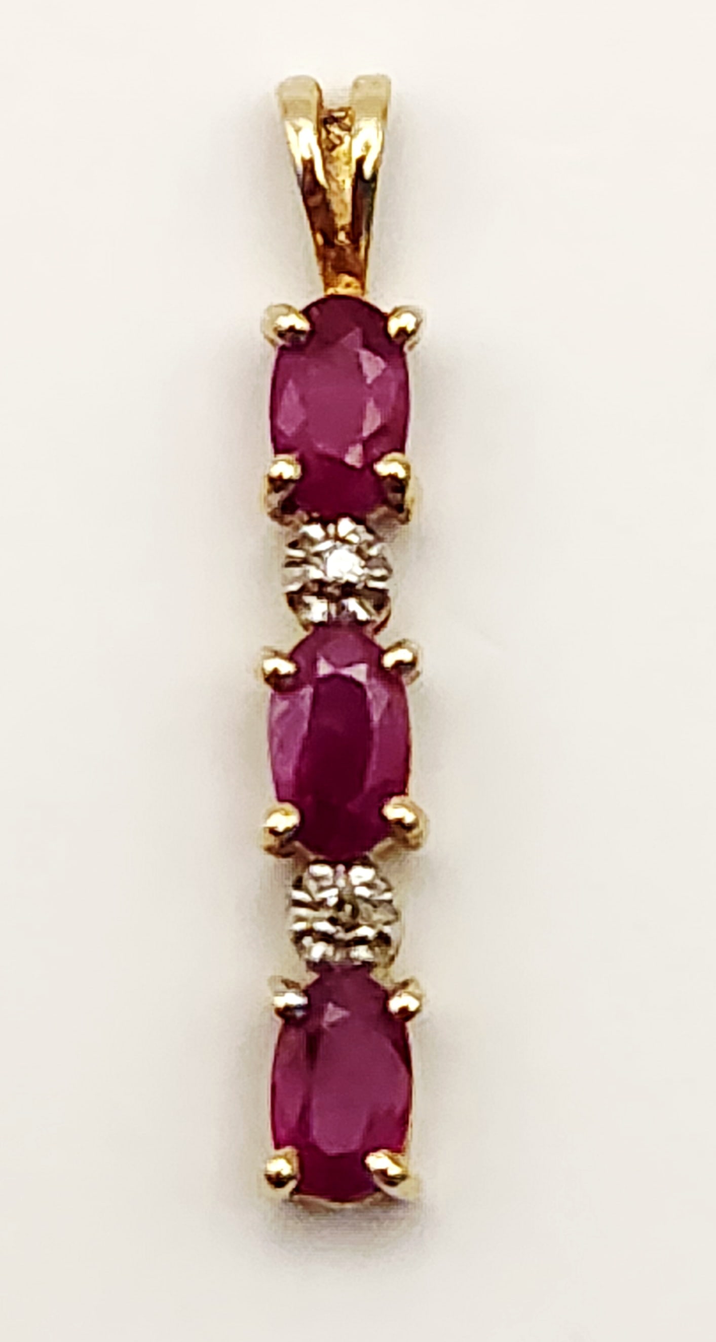 10K Gold Ruby Pendant 1.0 Gram: This vertical drop pendant is constructed in 10 karat yellow gold. The reverse of the bail is stamped with a 10K purity mark. Total length: Approximately 1 inch Weight: Approximately 1.0 gram. The ite