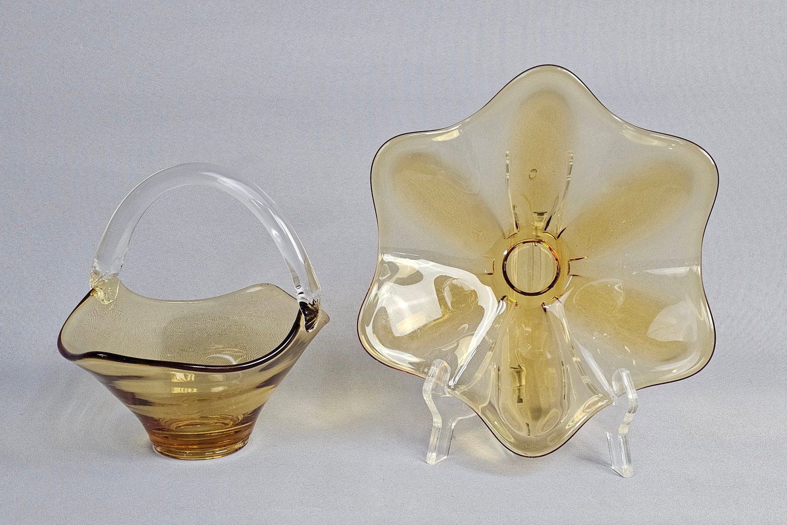 Two Pieces of Mid-Century Amber Art Glass Including a Fluted Bowl and Handled Basket: This lot features two pieces of transparent amber art glass, likely of mid-20th-century American origin. The first piece is a low fluted bowl with a six-lobed flower-form rim, resembling the Epic line