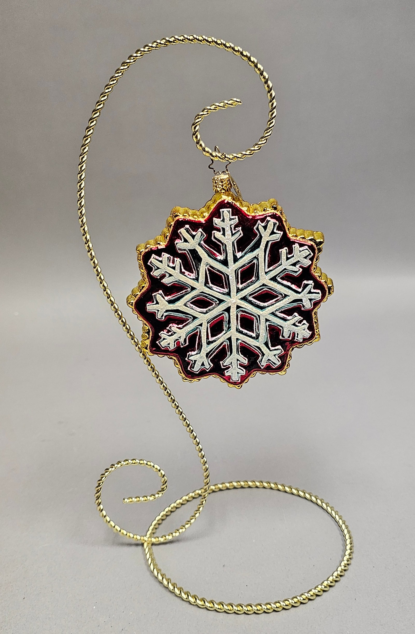 Patricia Breen Designs Hand-Blown Glass Snowflake Christmas Ornament: Stand not included. A hand-blown glass Christmas ornament by Patricia Breen Designs, shaped as a multi-pointed snowflake. The ornament features a deep red translucent glass ground decorated with an in