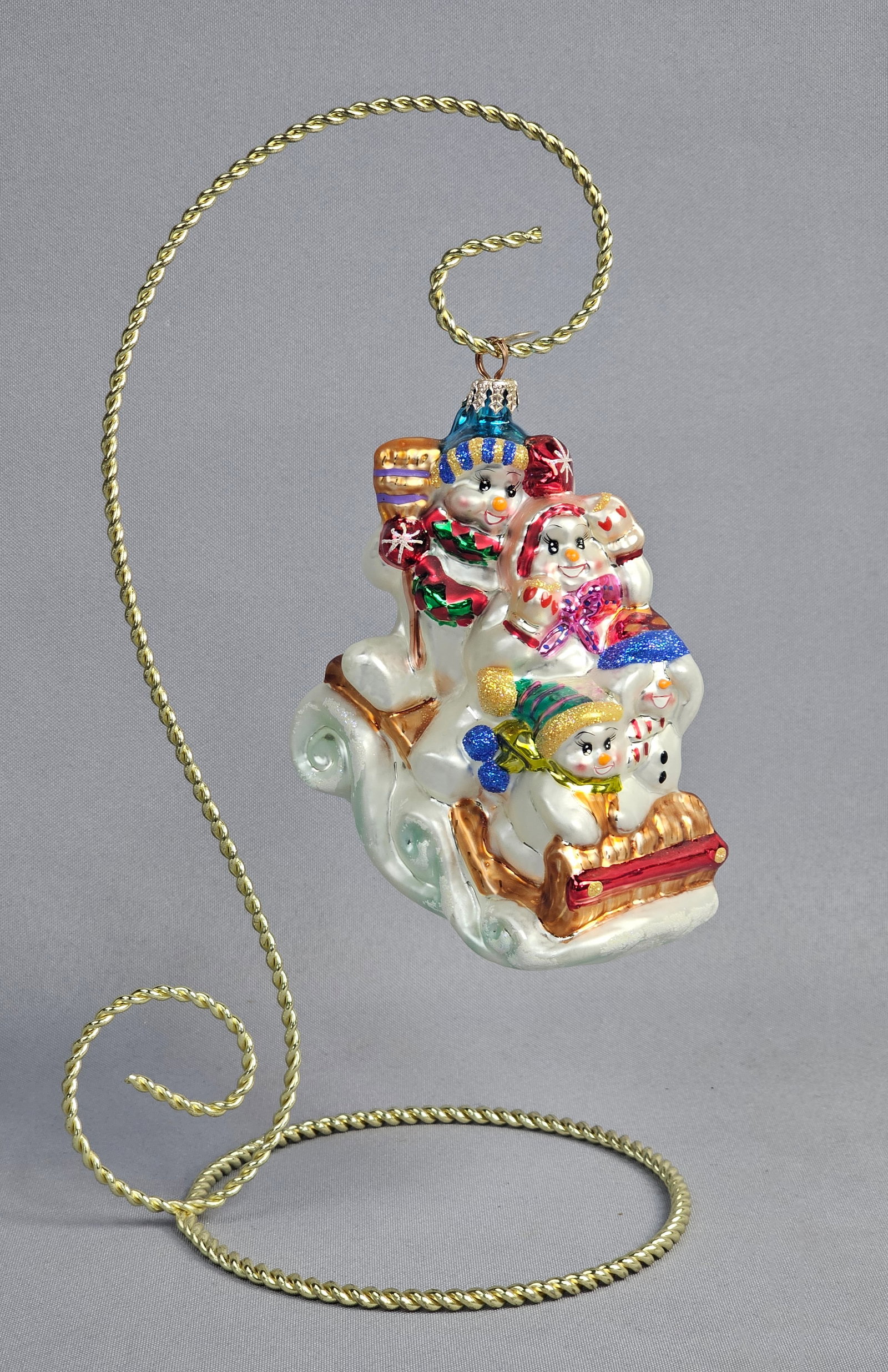 Christopher Radko Snowman Sledding Party Glass Christmas Ornament: Stand not included. A Christopher Radko hand-painted blown glass Christmas ornament titled Snowman Sledding Party. The ornament features a group of four snowmen wearing colorful winter hats and scarve