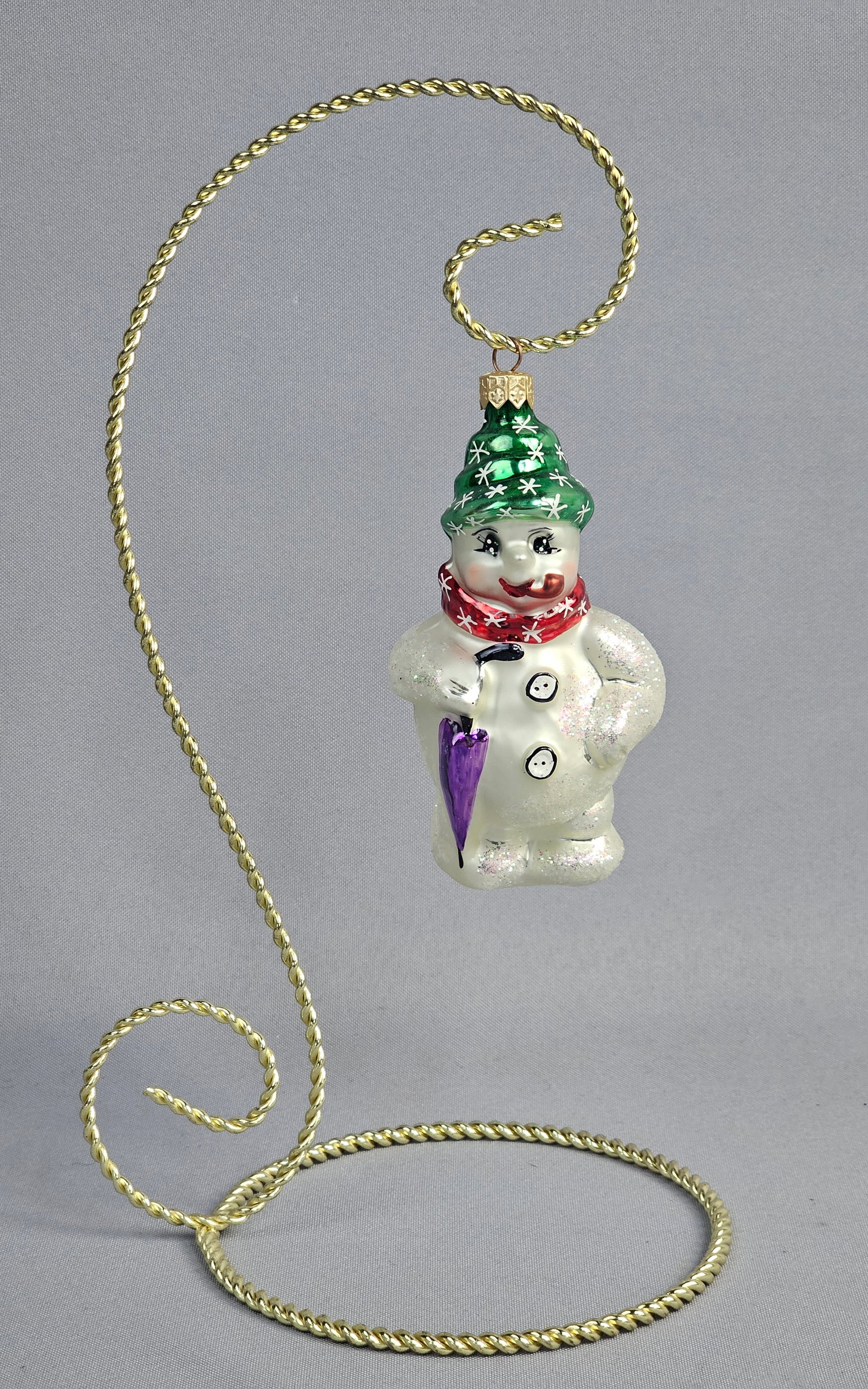 Christopher Radko Glass Snowman Ornament: Stand not included. This mouth-blown and hand-painted glass Christmas ornament is produced by Christopher Radko. The whimsical snowman figure is wearing a green conical hat shaped like a stylized ever