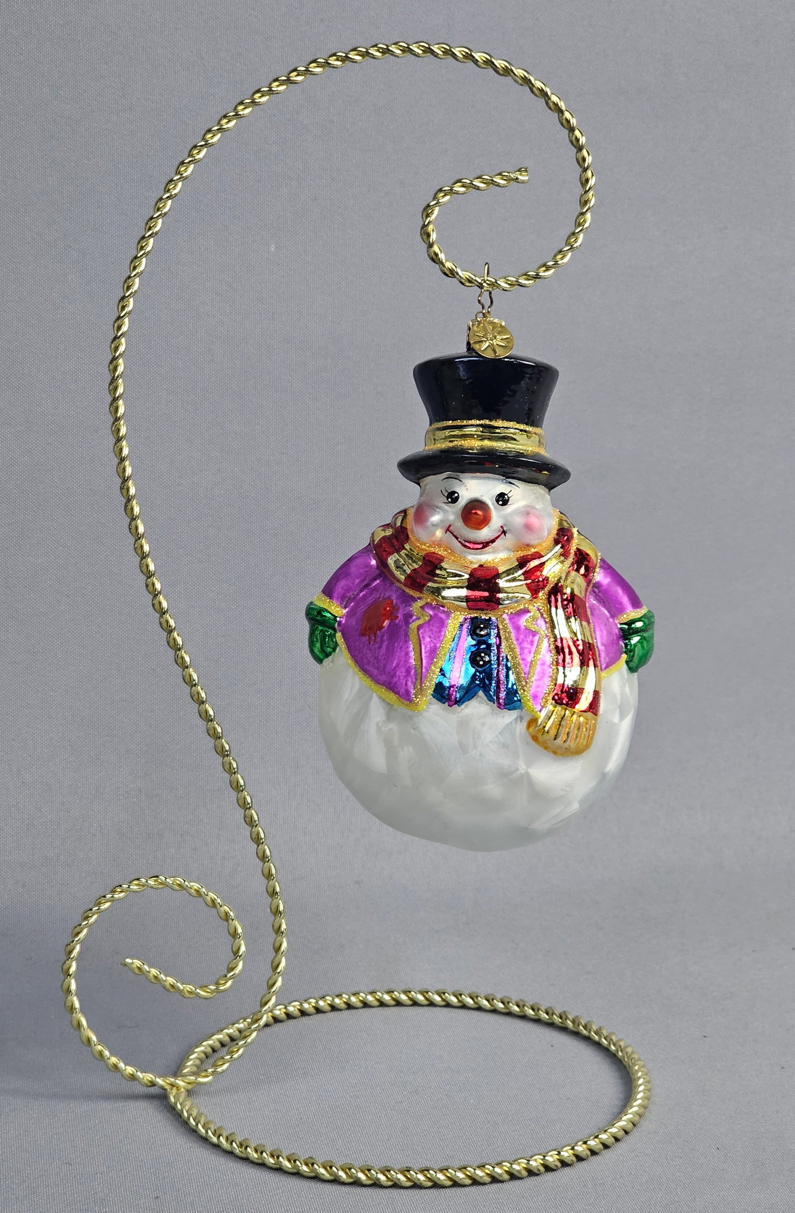 Christopher Radko Hand-Blown Glass Snowman Christmas Ornament: Stand not included. A Christopher Radko hand-blown glass Christmas ornament depicting a snowman in festive attire. The figure is designed with a black top hat featuring gold glitter trim, a purple jac